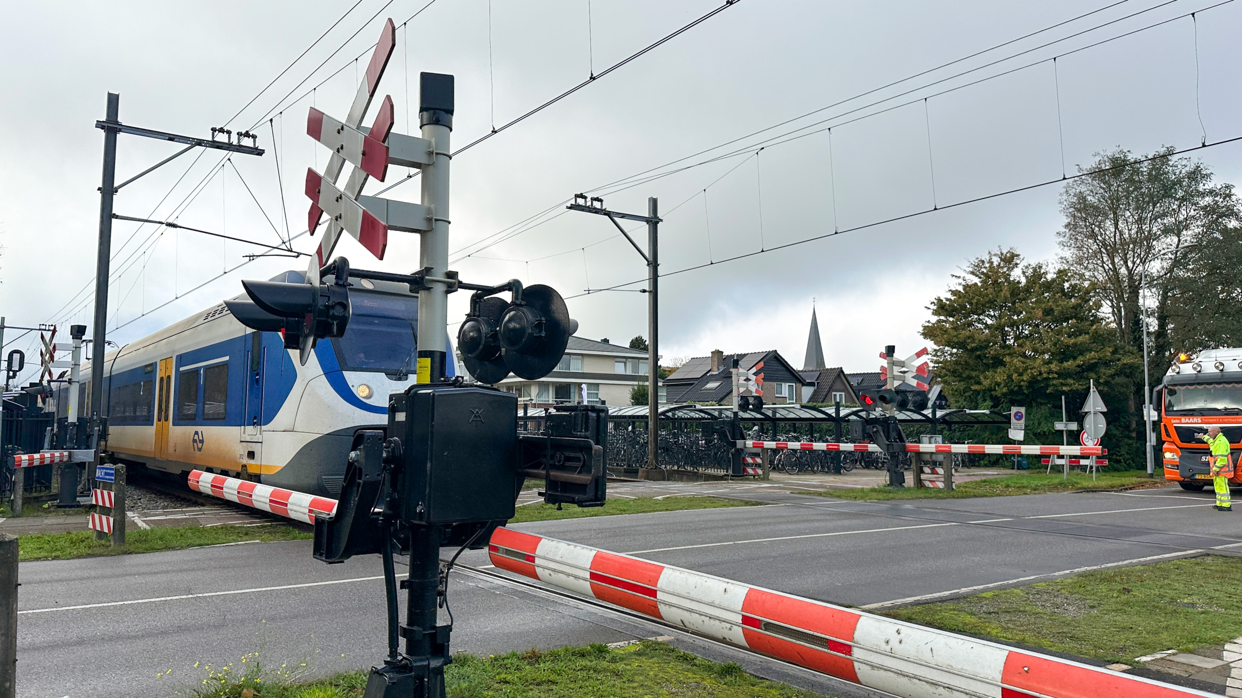 Een trein passeert een spoorwegovergang met gesloten slagbomen, terwijl een vrachtwagen wacht.