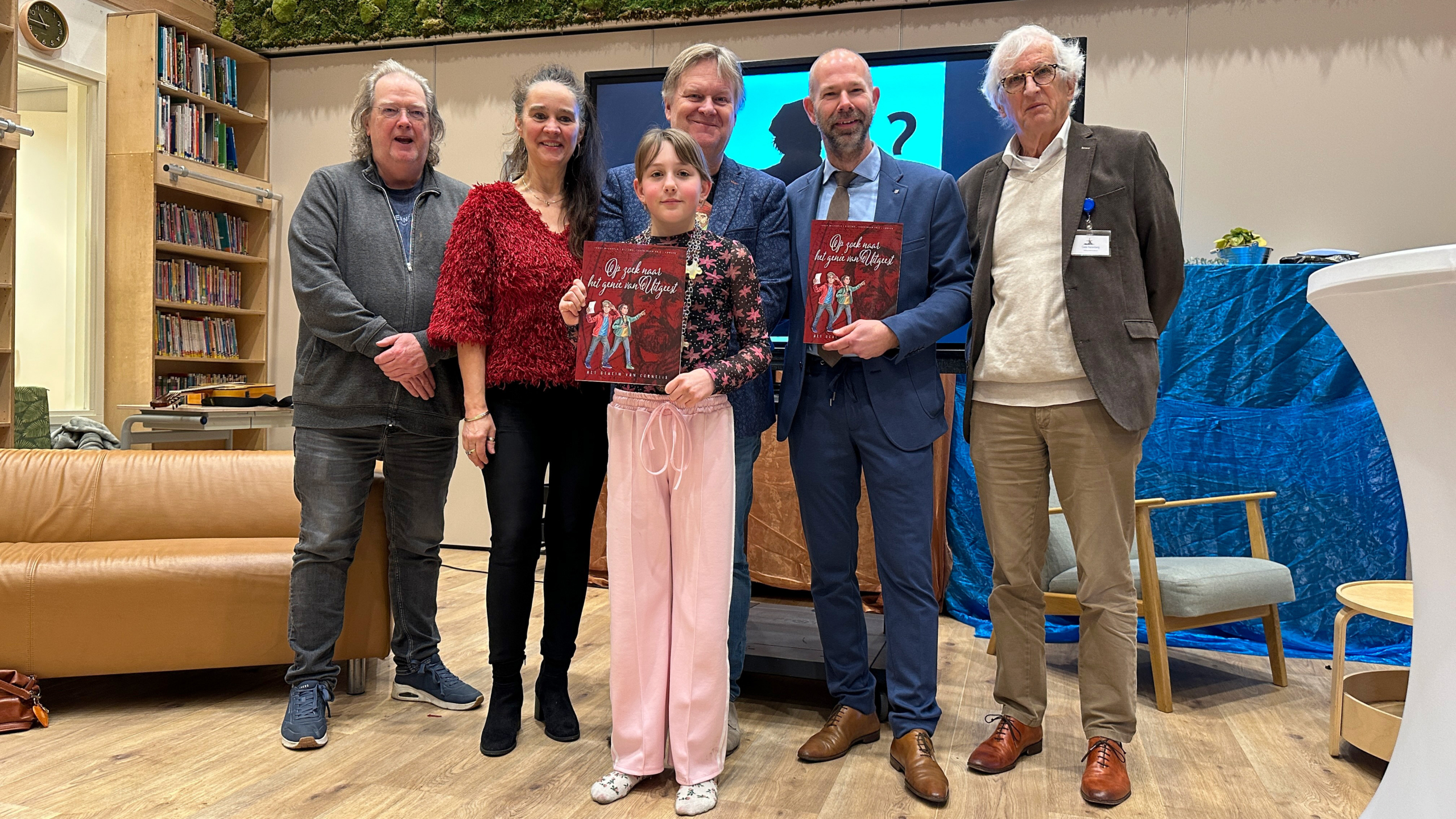 Zes mensen poseren binnen in een ruimte, twee van hen houden boeken vast met de titel "Op zoek naar het spoor van...".