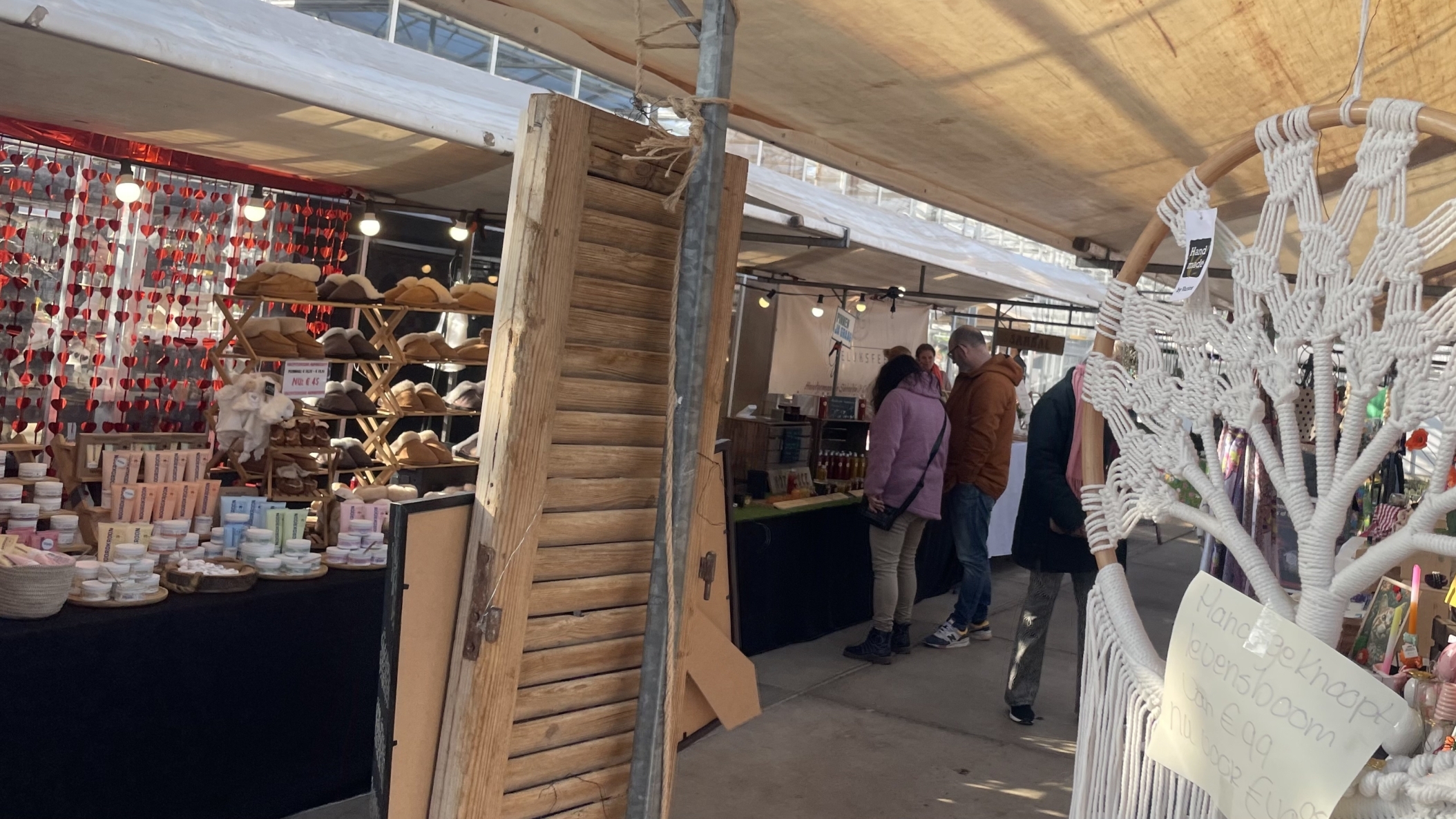 Marktkraam met handgemaakte levensboomdecoratie en producten op een tafel, mensen bekijken de kraam.