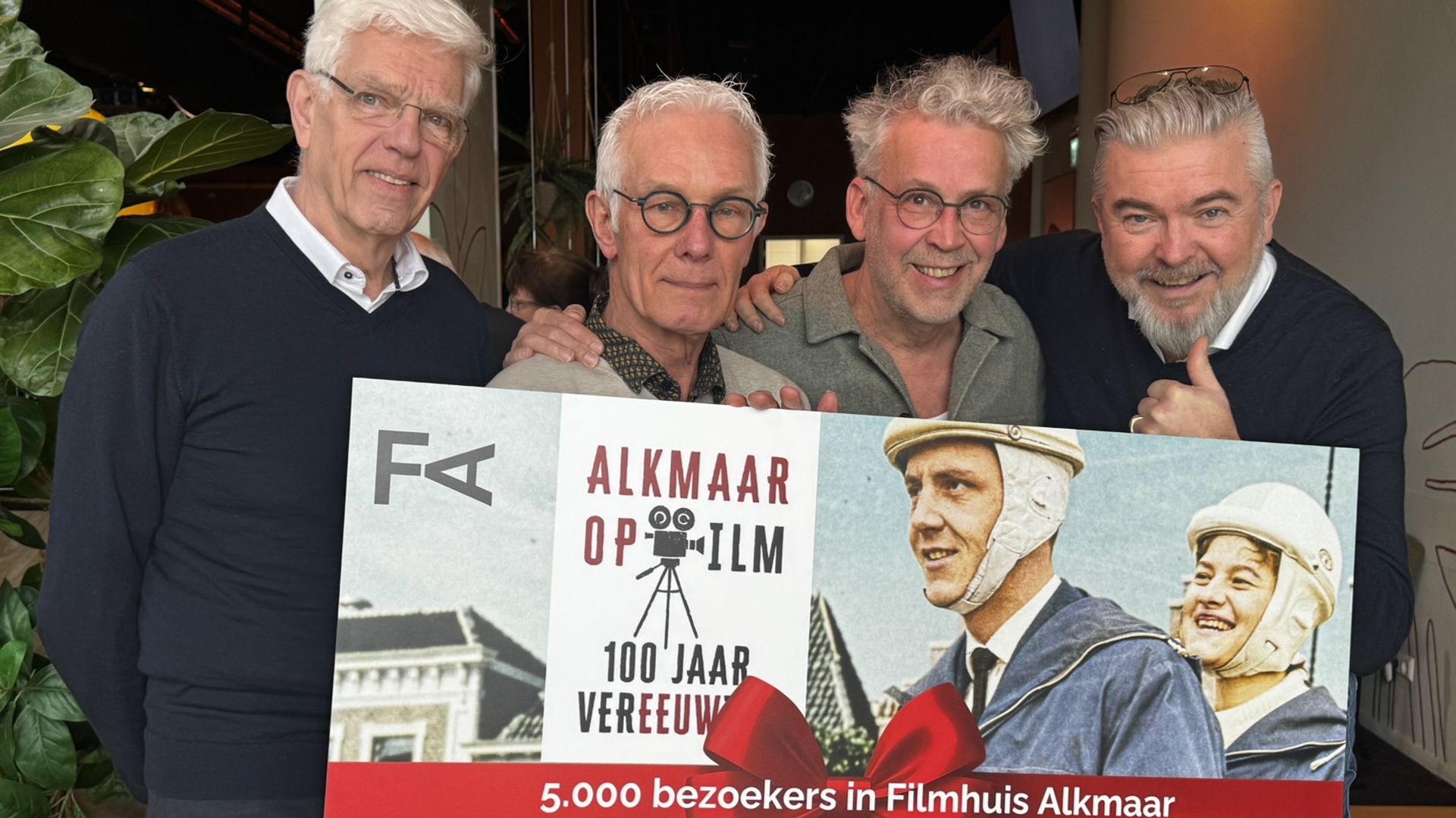 Vier mannen poseren met een poster van "Alkmaar op Film" voor 5.000 bezoekers in het Filmhuis Alkmaar.