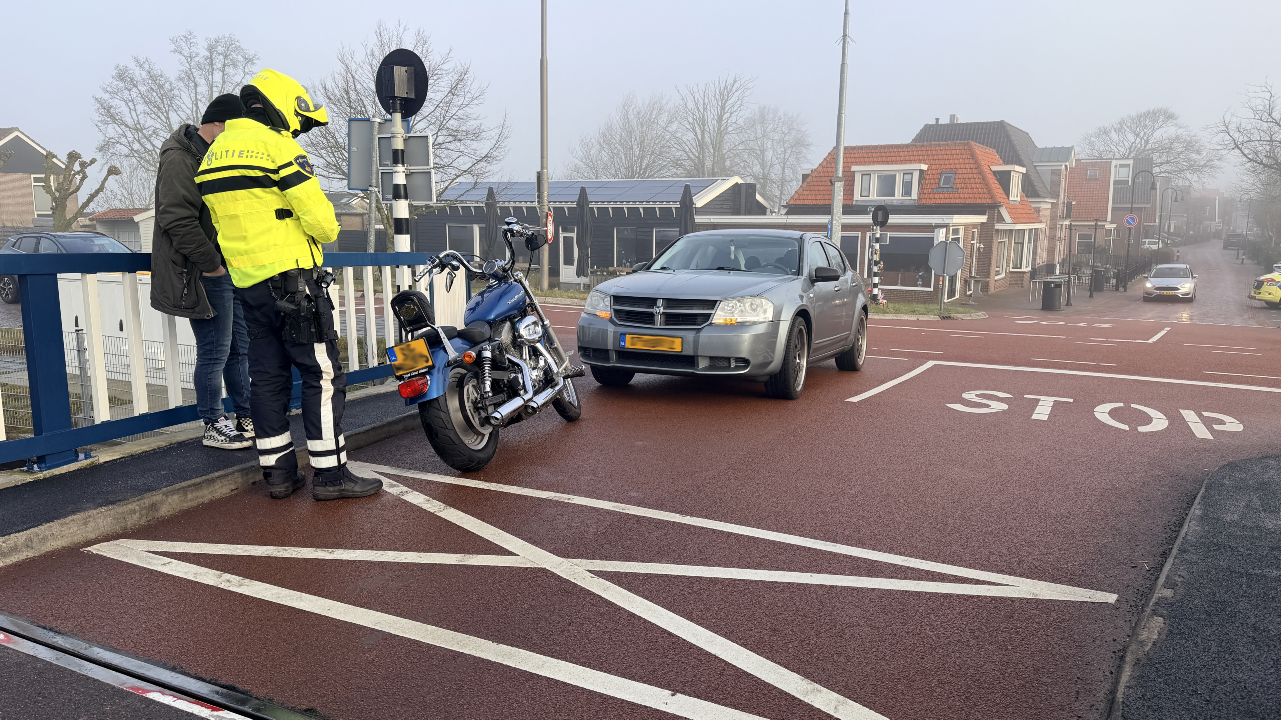 Een politieagent in geel uniform spreekt een man aan naast een geparkeerde motorfiets, met een auto op de achtergrond.