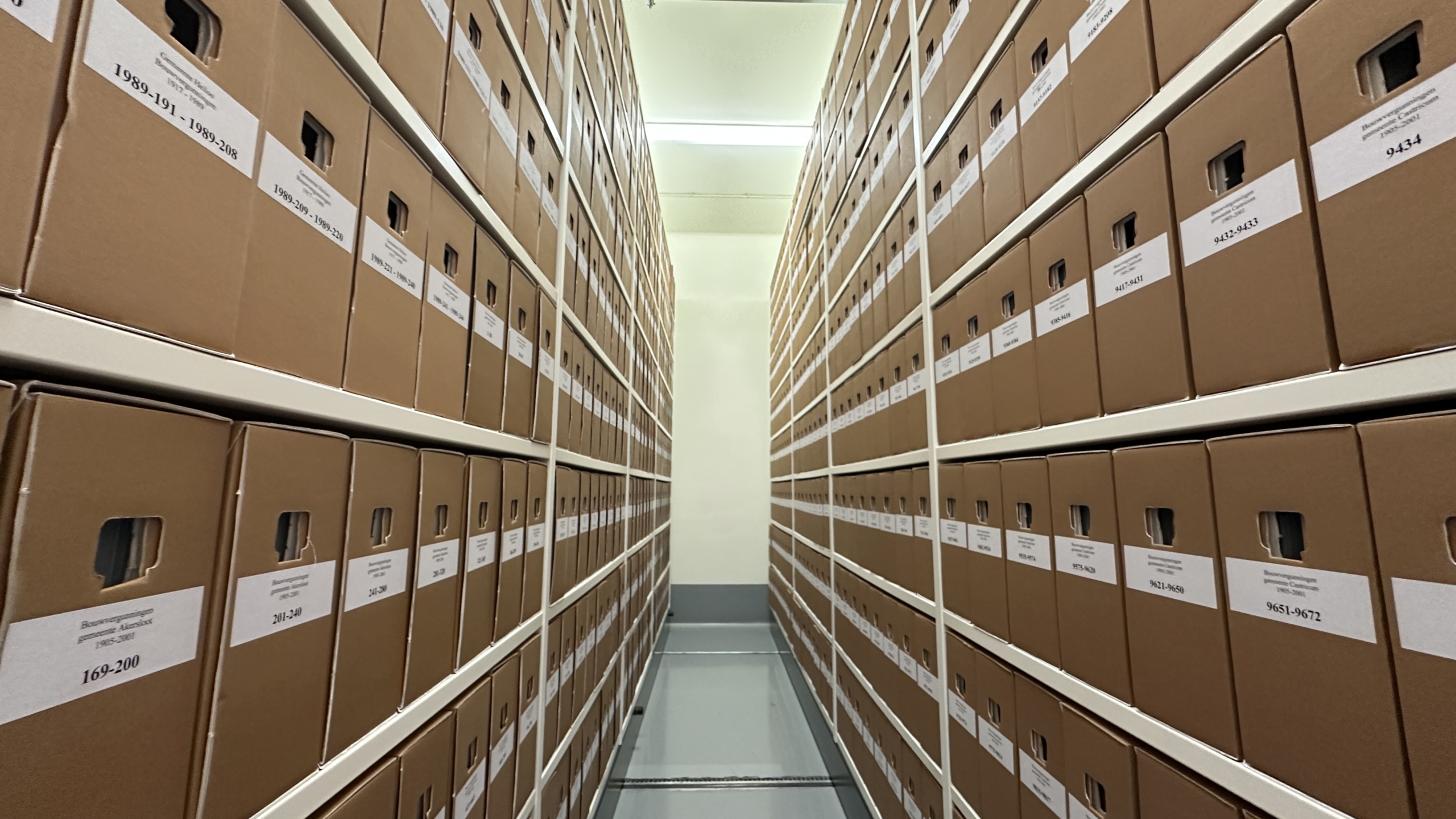 Gang met archiefdozen netjes gestapeld in hoge rekken aan beide kanten.