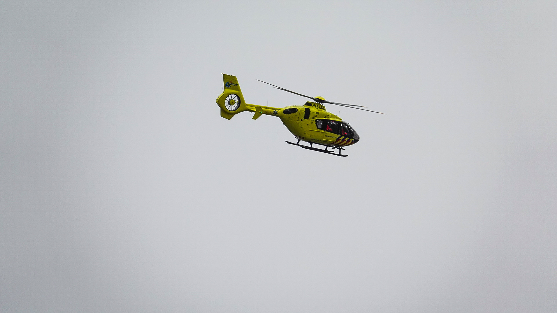 Gele traumahelikopter vliegt door een grijze lucht.