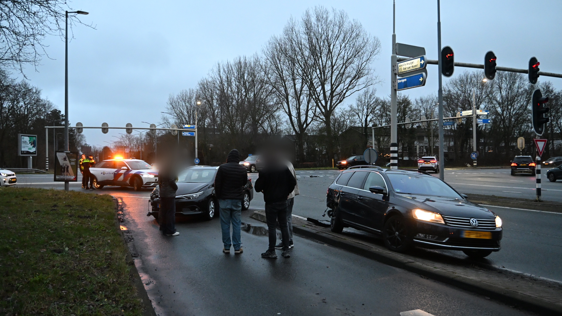 Verkeersongeval op kruispunt met politieauto en meerdere betrokken auto's op een regenachtige dag.