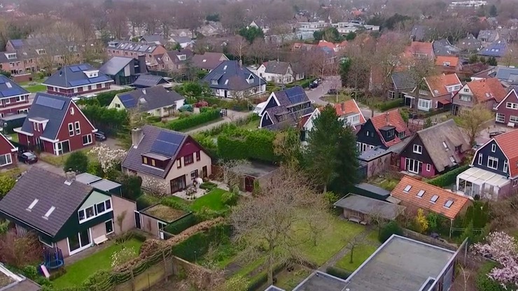 Luchtfoto van een woonwijk met verschillende vrijstaande huizen, omgeven door bomen en tuinen.