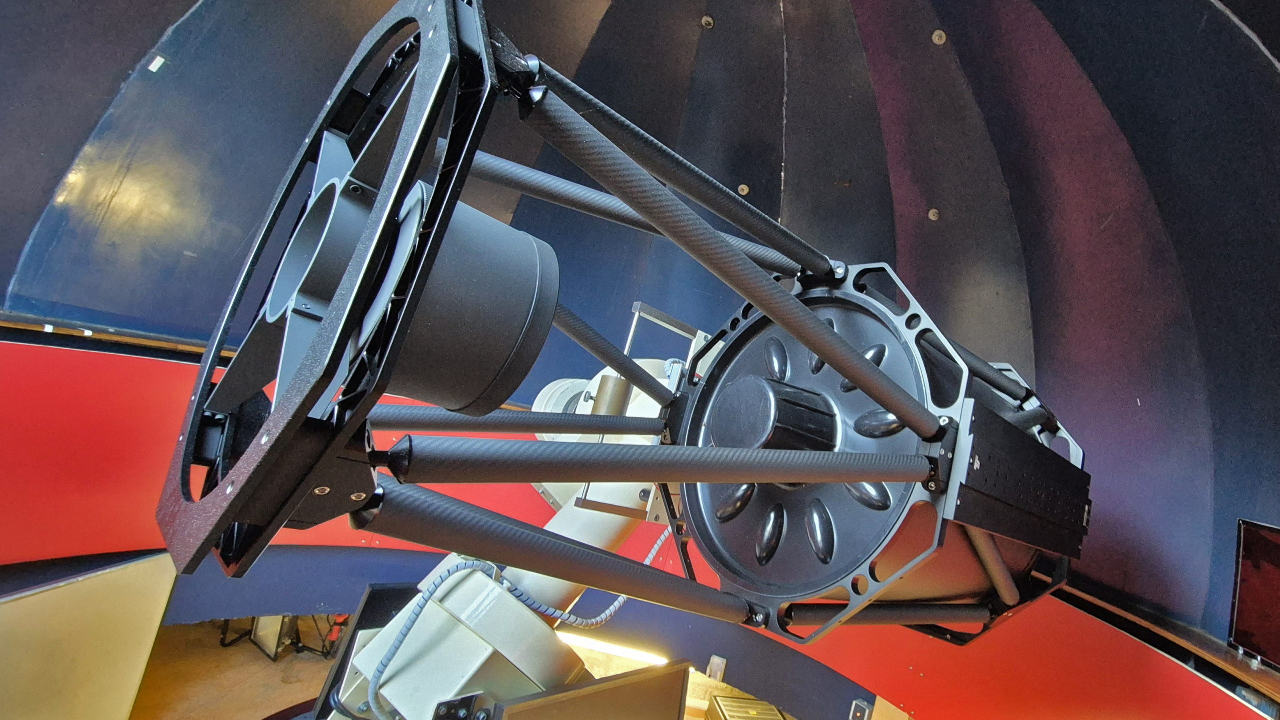 Een grote telescoop met een complexe structuur in een observatorium met gekleurde muren.