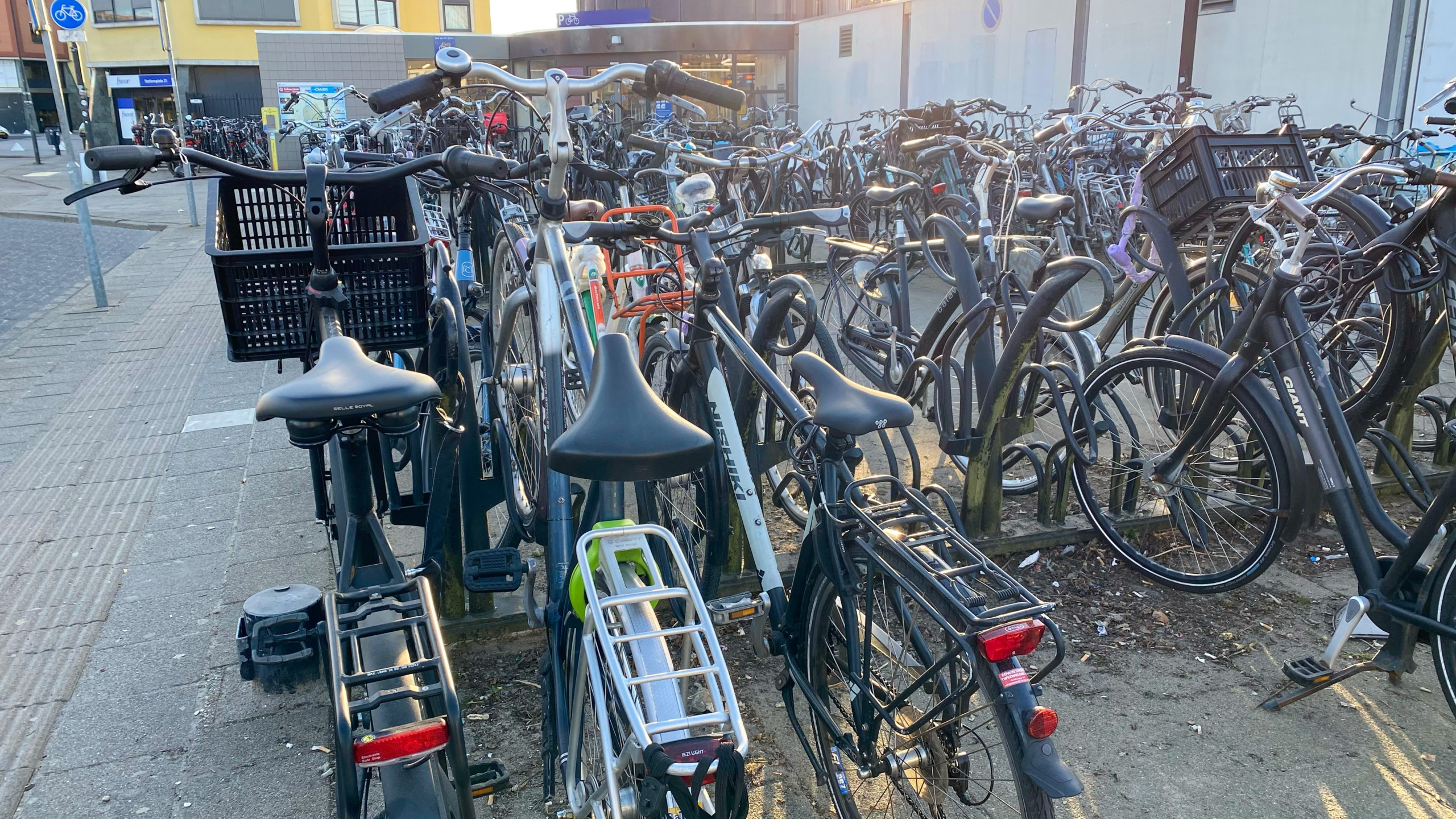 Veel fietsen geparkeerd in een rek op een trottoir in een stedelijke omgeving.