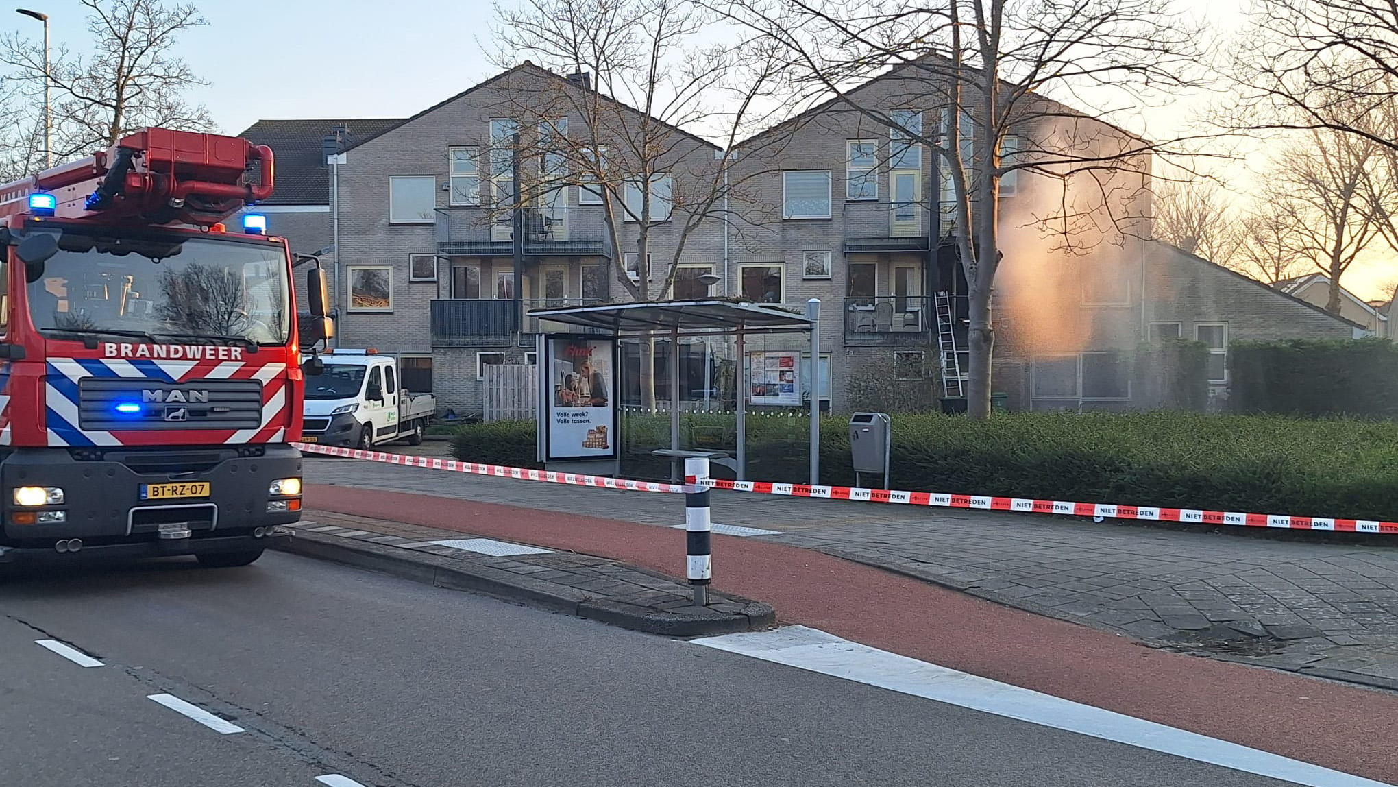 Brandweerwagen bij appartementencomplex met afzetlint en waterschade zichtbaar op gevel.