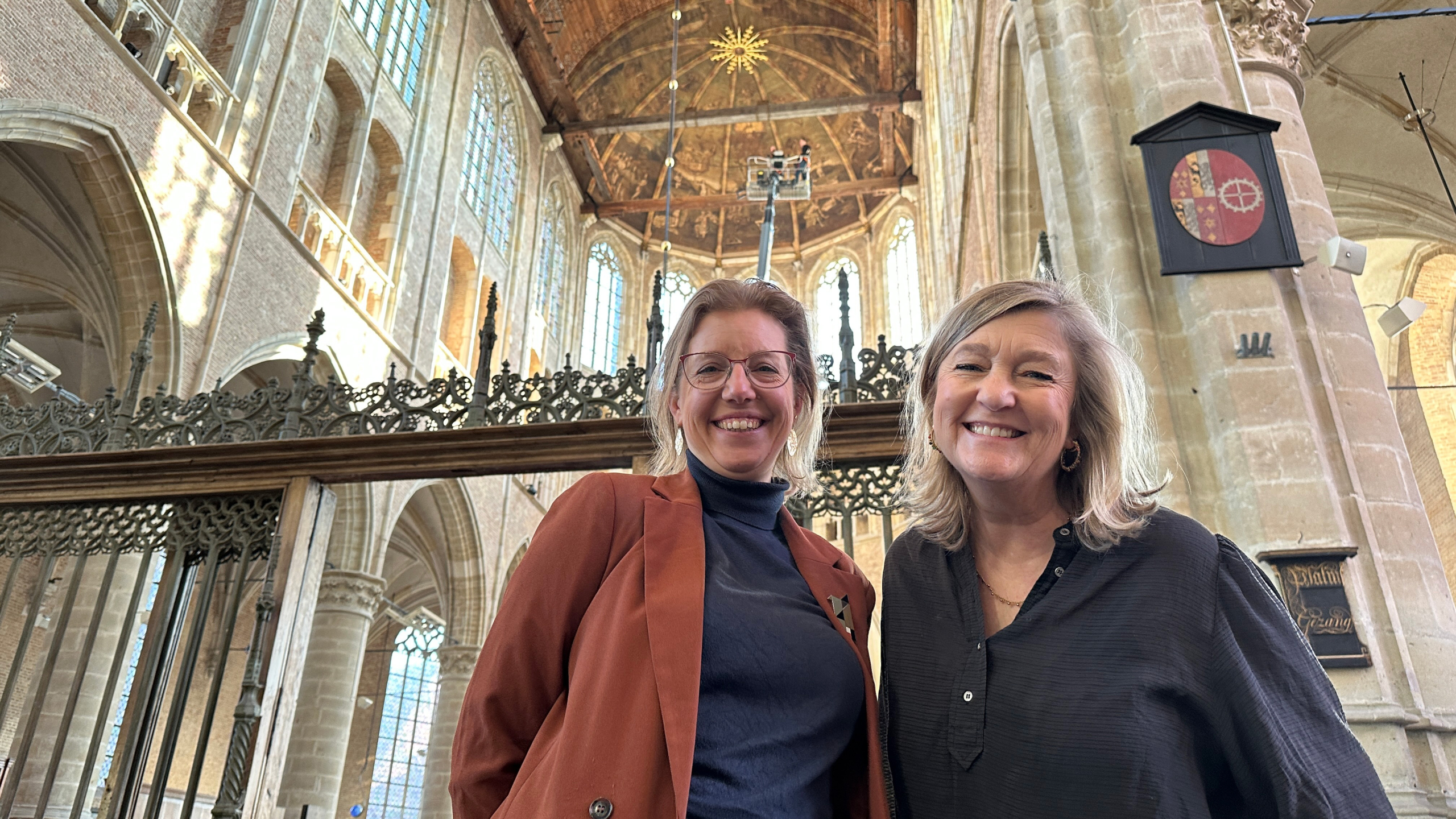 Twee vrouwen glimlachen in een historische kerk met hoge gewelfde plafonds en sierlijke ramen.