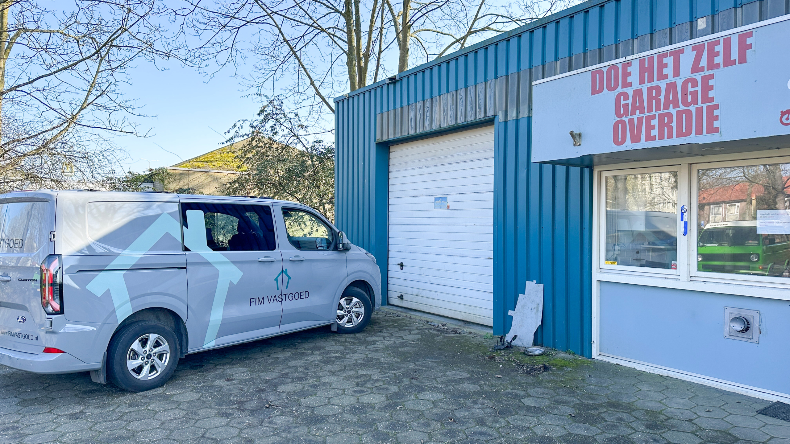 Busje van FIM Vastgoed geparkeerd naast een blauw gebouw met het bord "Doe Het Zelf Garage Overdie".