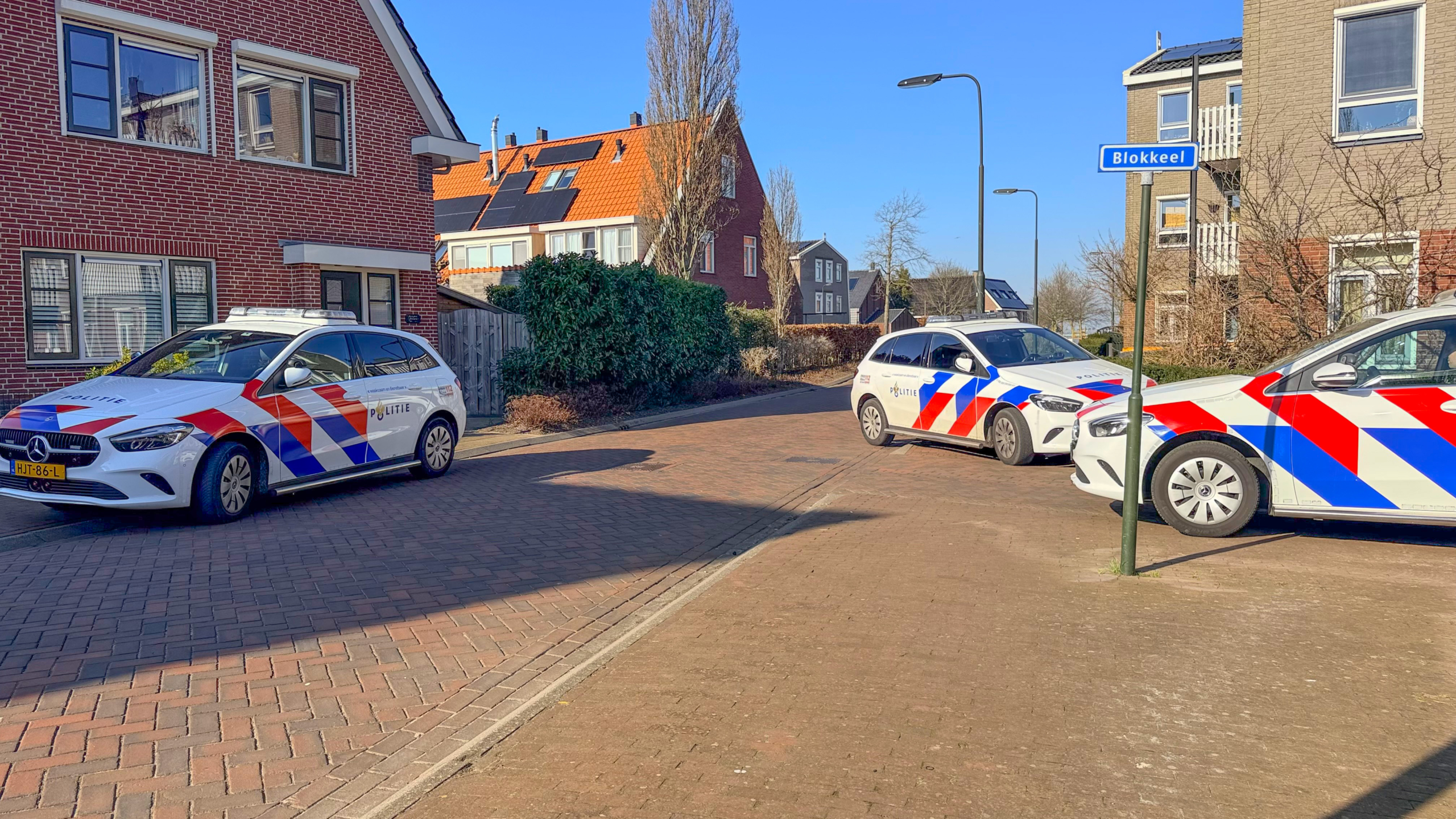Drie politieauto's staan geparkeerd in een woonwijk naast een straatnaambord met "Blokkeel".