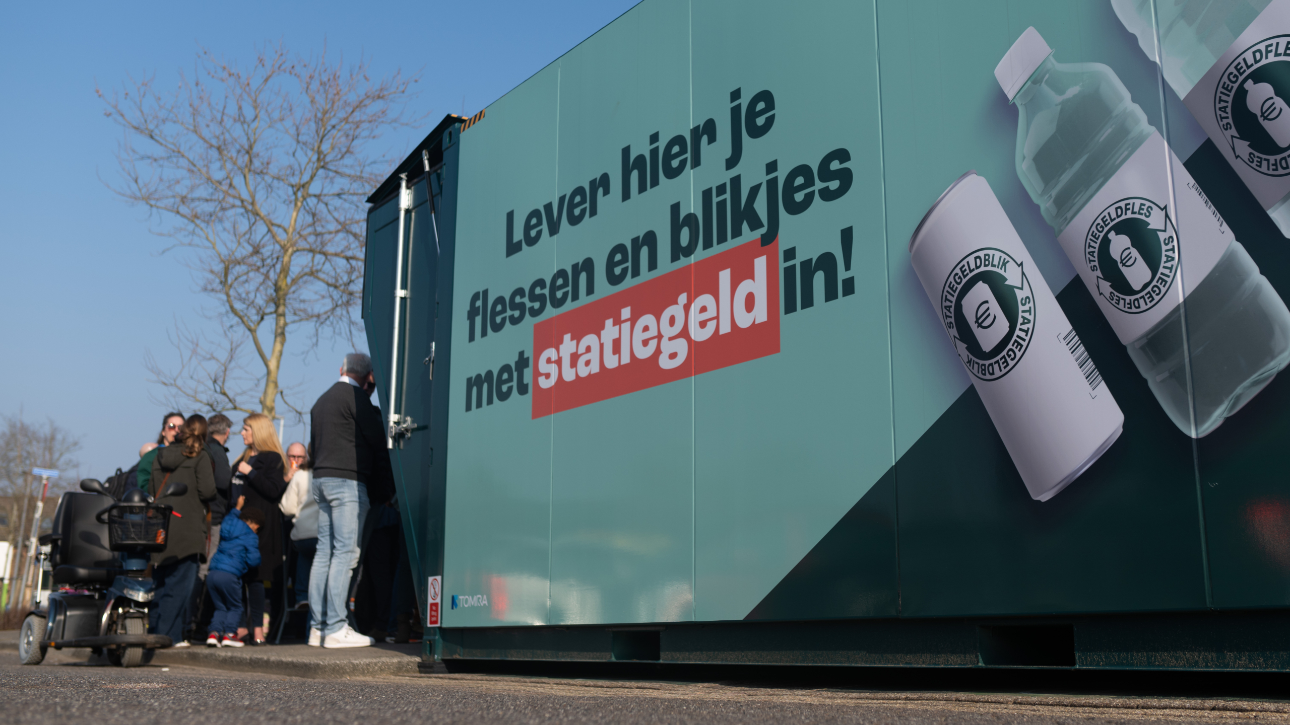 Container met de tekst "Lever hier je flessen en blikjes met statiegeld in!" en mensen die buiten wachten.