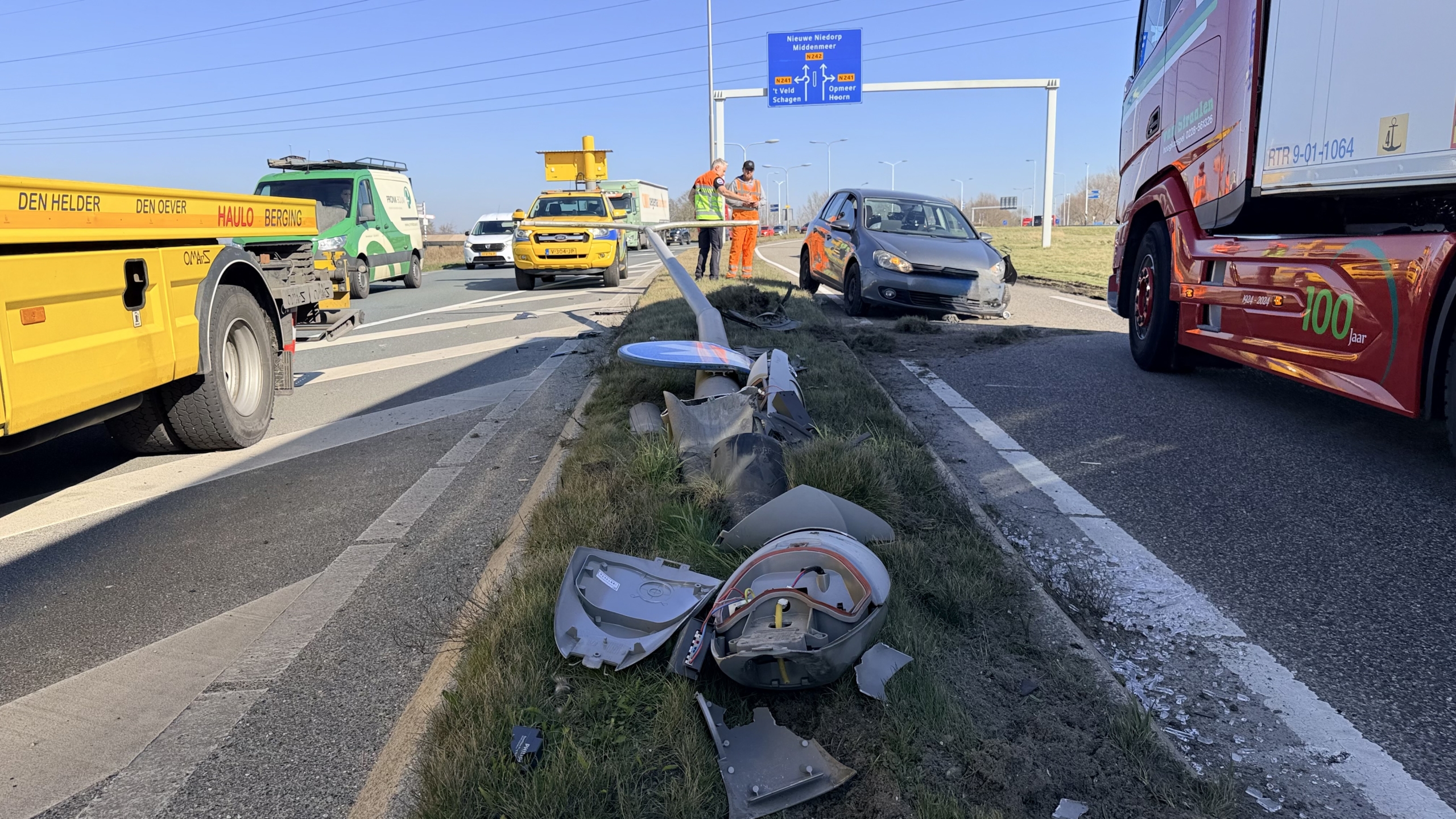 Verkeersongeval op een snelweg met een beschadigde auto en omgevallen lantaarnpaal, omringd door bergingsvoertuigen.