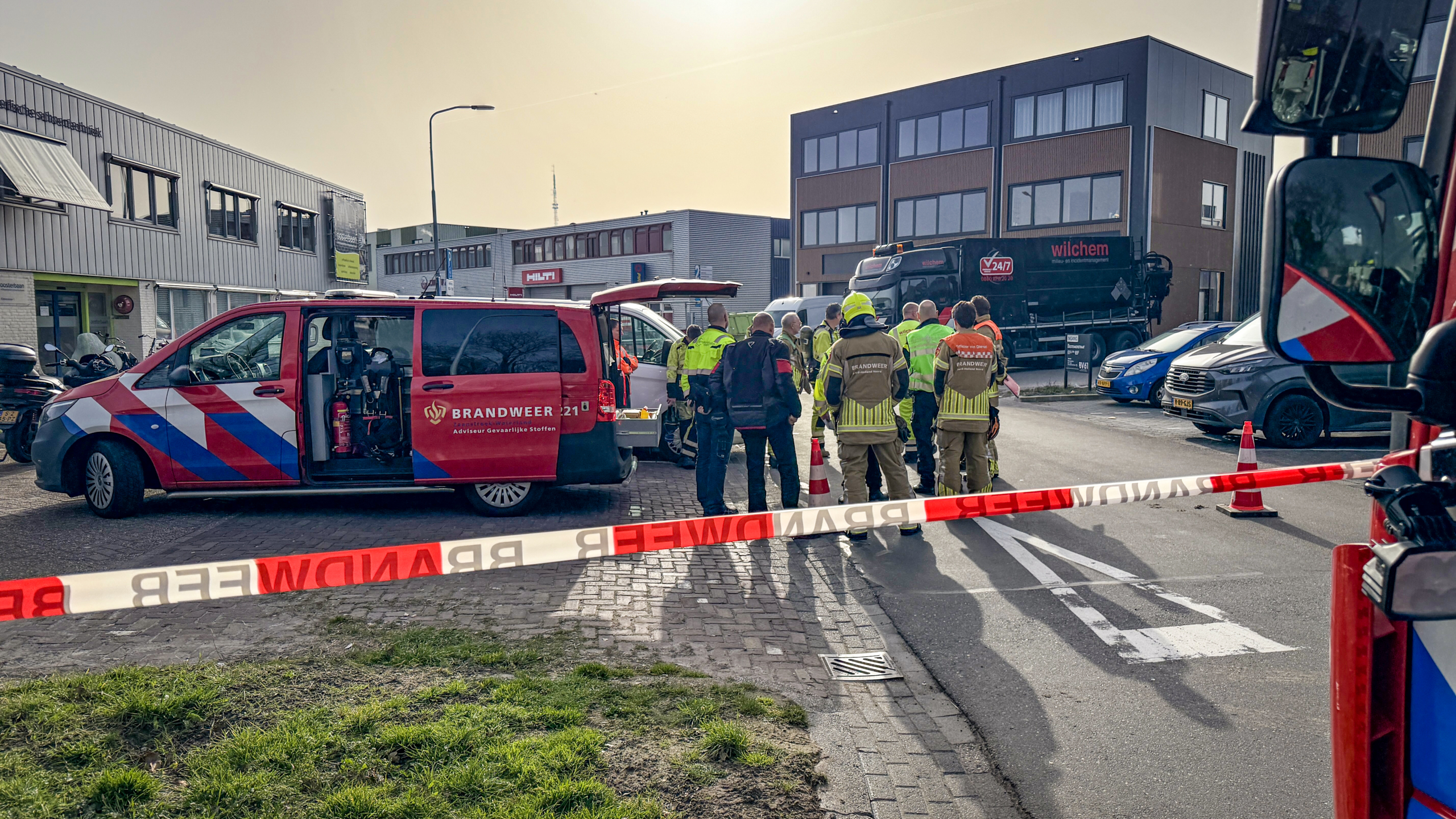 Brandweer en politie staan bij afgesloten gebied met brandweerauto's in een stedelijke omgeving.