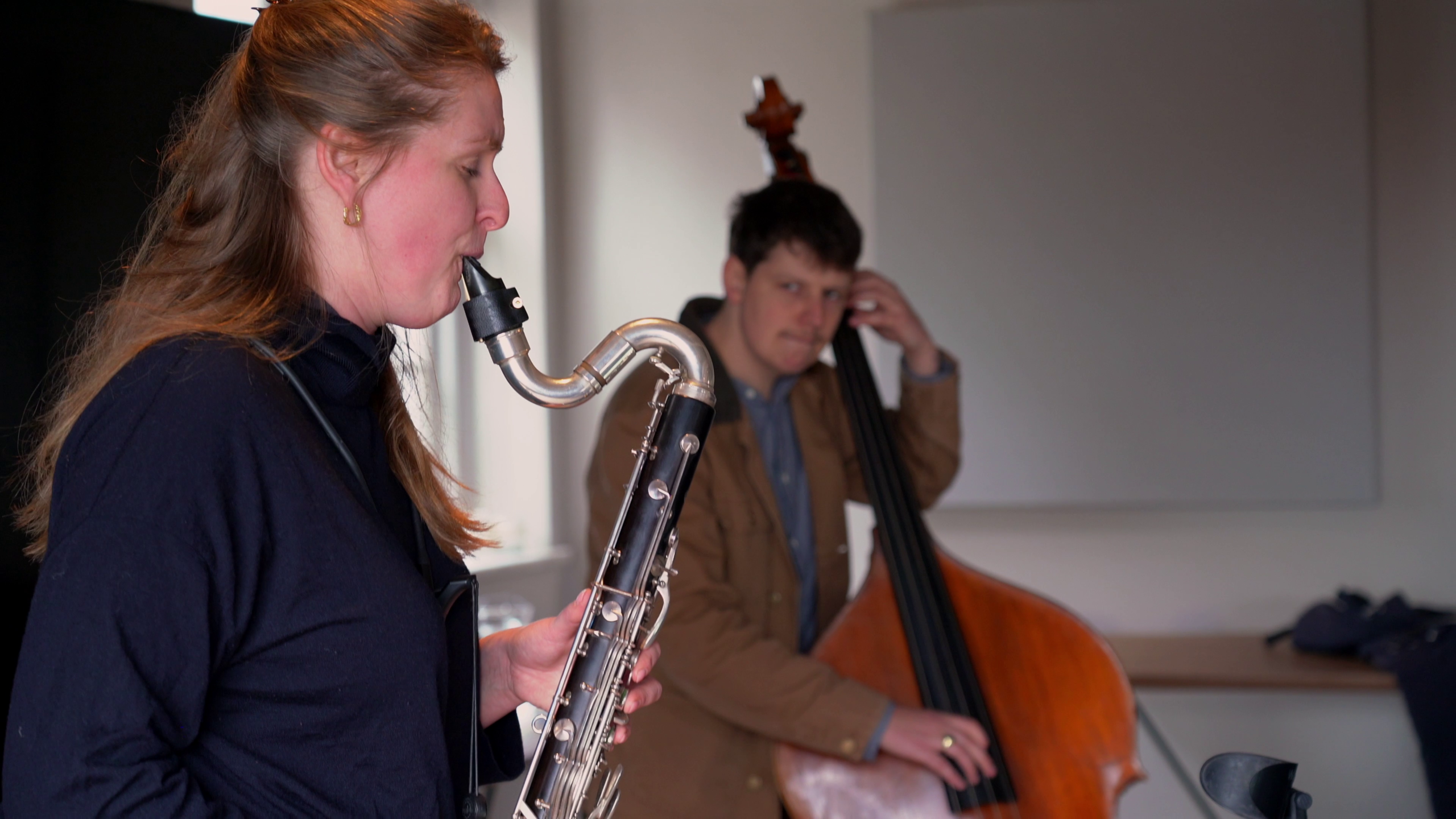 Een vrouw speelt klarinet en een man speelt contrabas in een kamer.