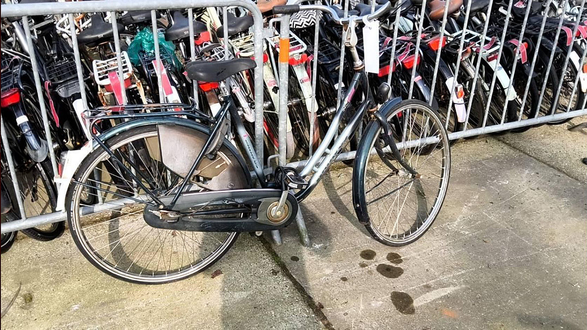 Een beschadigde fiets tegen een hek met meerdere fietsen erachter geparkeerd.
