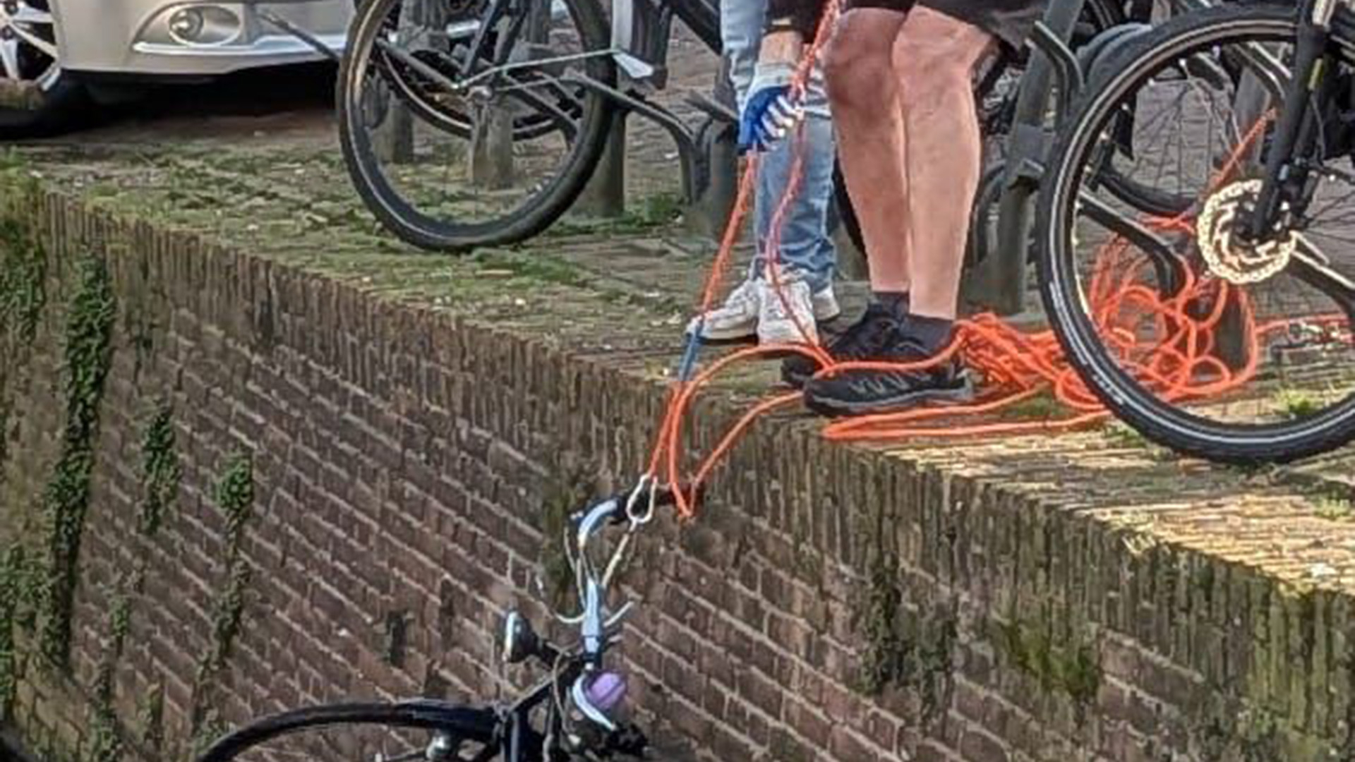 Twee mensen trekken een fiets uit een gracht met behulp van een oranjekleurig touw.