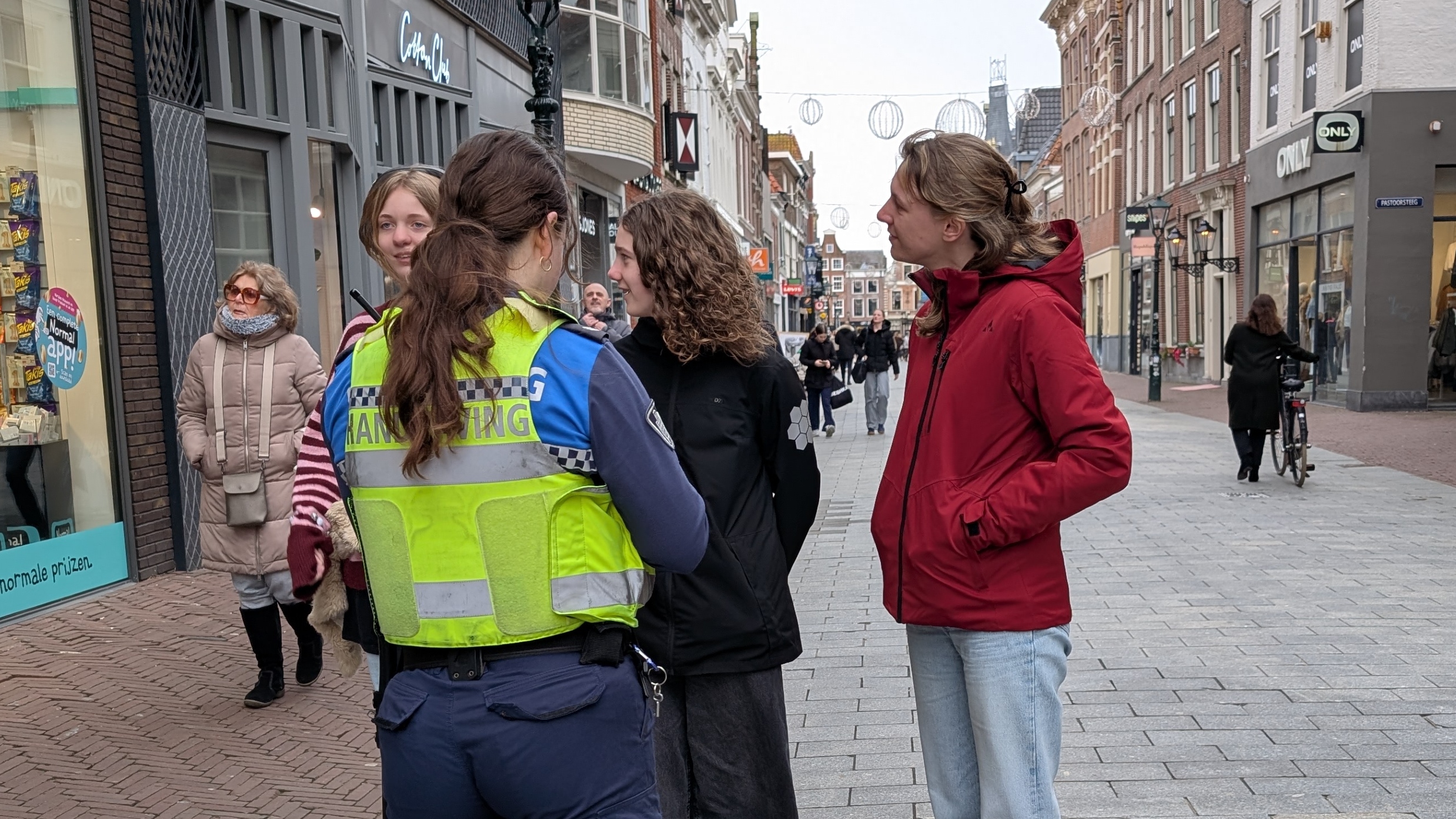 Een handhaver praat met twee personen op een winkelstraat, omringd door voorbijgangers.