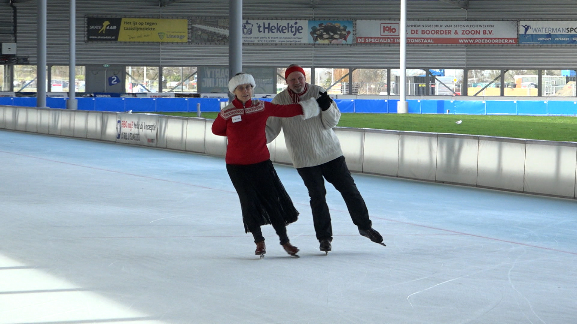 Twee personen schaatsen samen op een ijsbaan, gekleed in warme kleding en mutsen.
