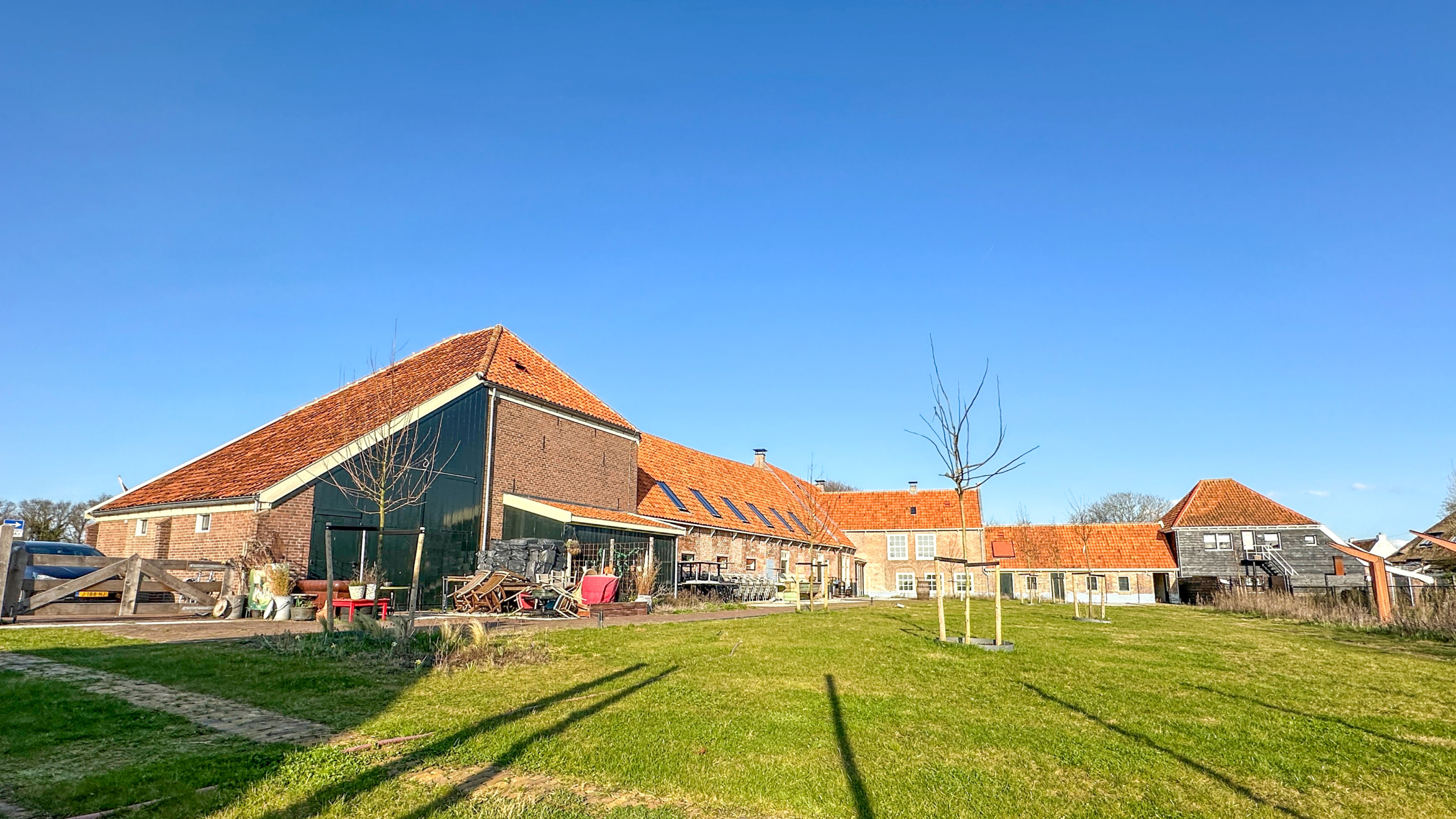 Een boerderij met rode daken en een groene gevel, omgeven door een grasveld onder een heldere blauwe hemel.