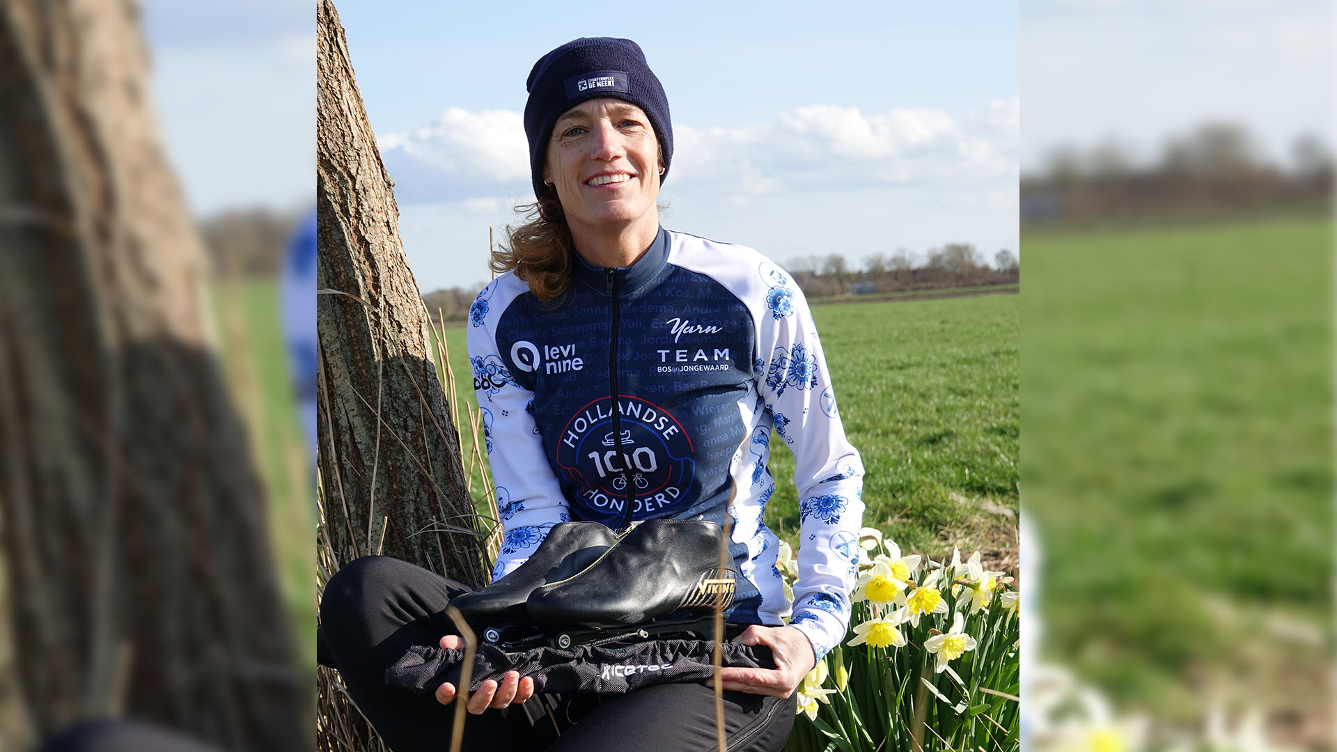 Persoon in sportkleding zit buiten bij een boom met schaatsen, omringd door groene velden en bloeiende narcissen.