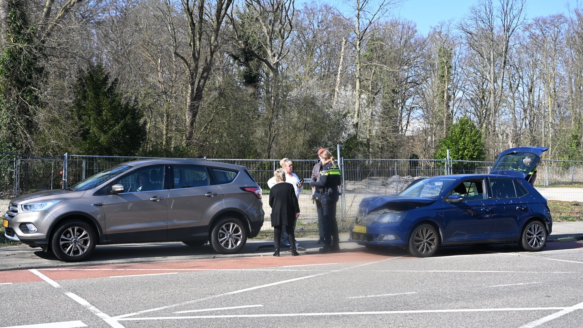 Twee auto's botsen op een weg met mensen die met een politieagent praten op de achtergrond.