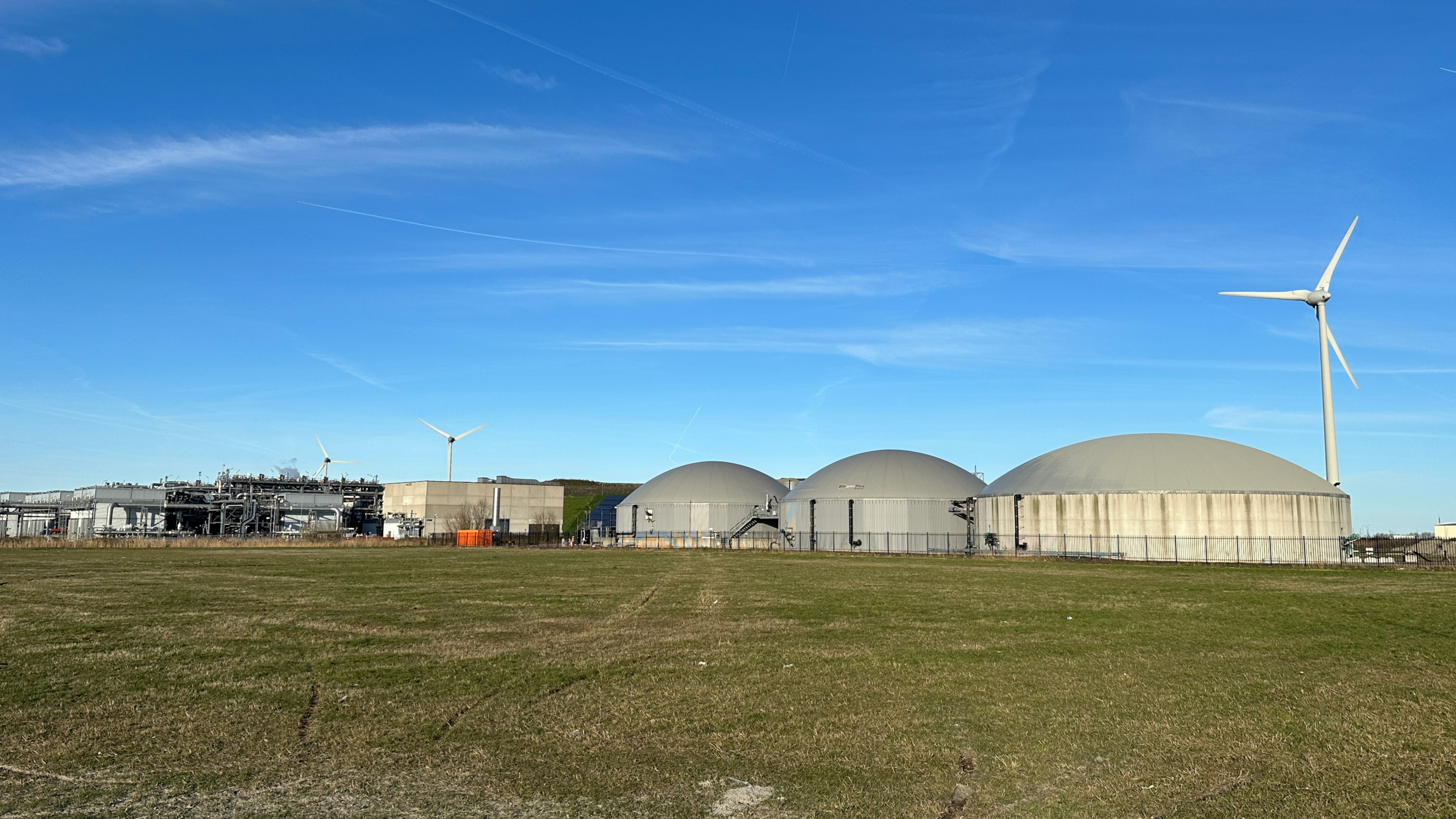 Industriële complex met koepelvormige tanks en windturbines tegen een heldere blauwe lucht.