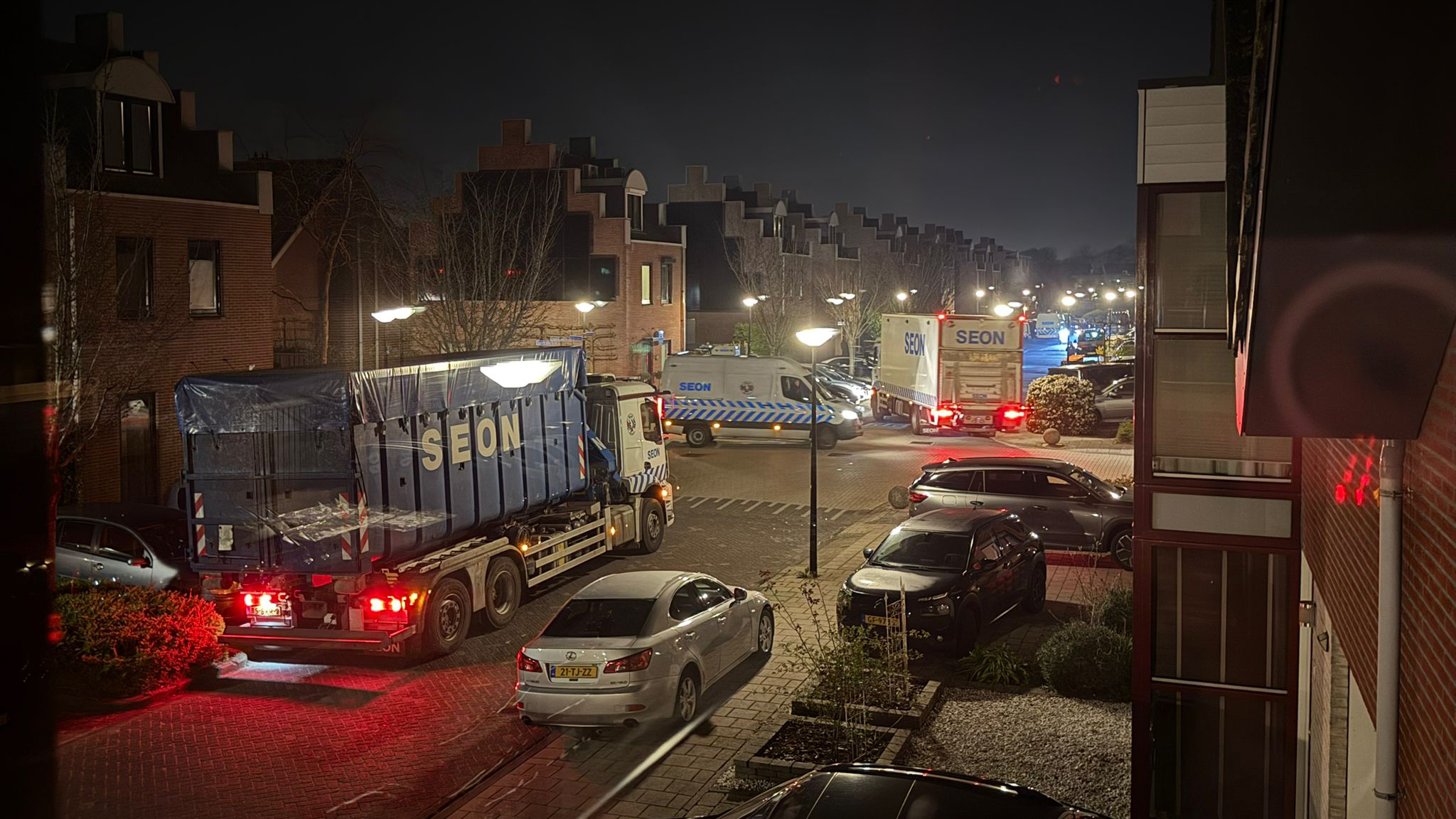 Vrachtwagens en bestelwagens met het logo "SEON" staan in een woonwijk 's nachts, verlicht door straatlantaarns.