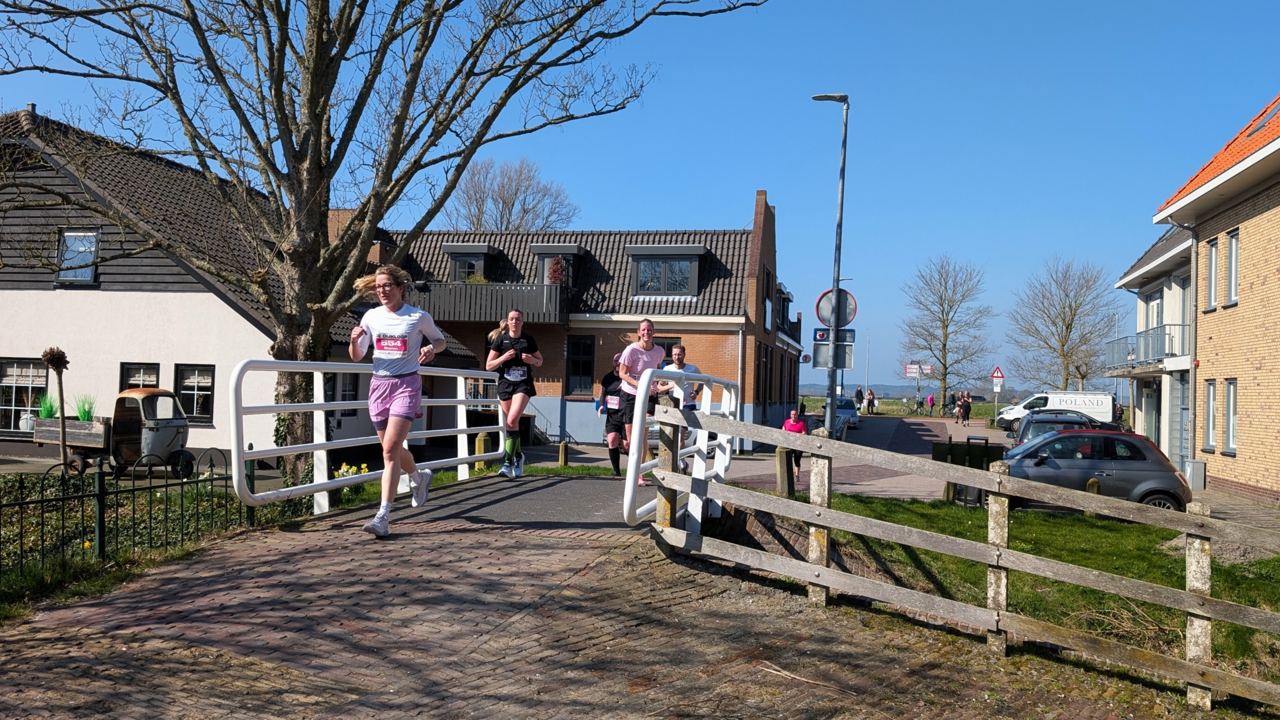 Mensen rennen over een brug in een woonwijk op een zonnige dag met een blauwe lucht.