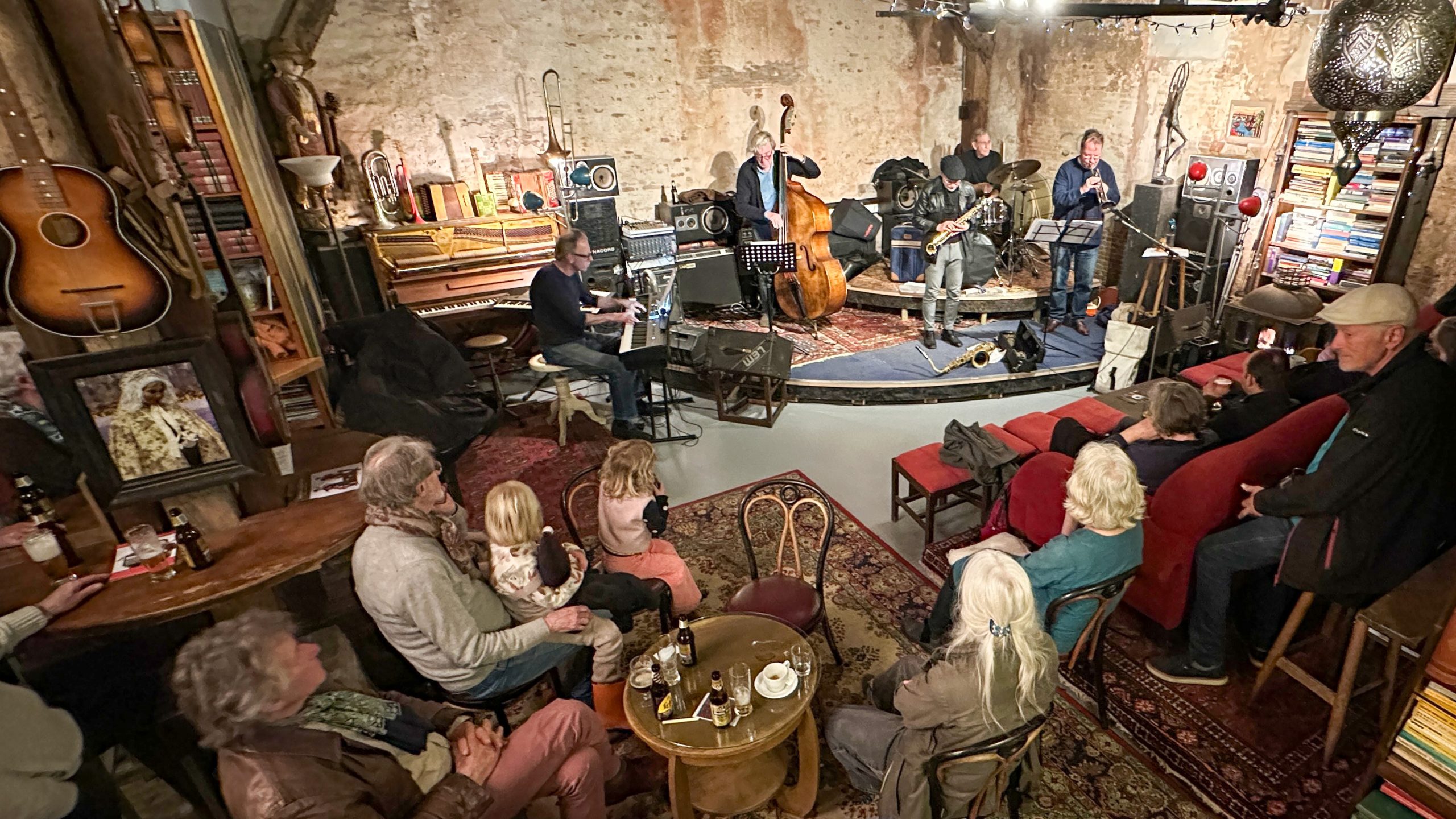 Mensen luisteren naar een live jazzband in een gezellige ruimte met boeken en muziekinstrumenten aan de muren.