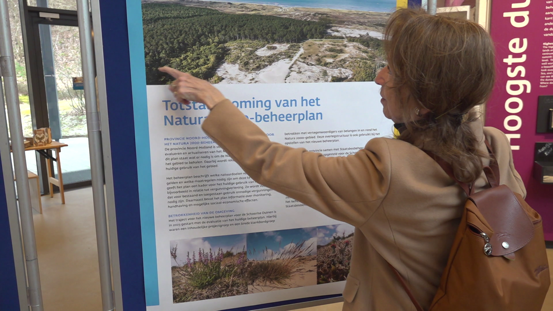 Een vrouw wijst naar een informatiepaneel over het Natura 2000-beheerplan met een foto en uitleg.