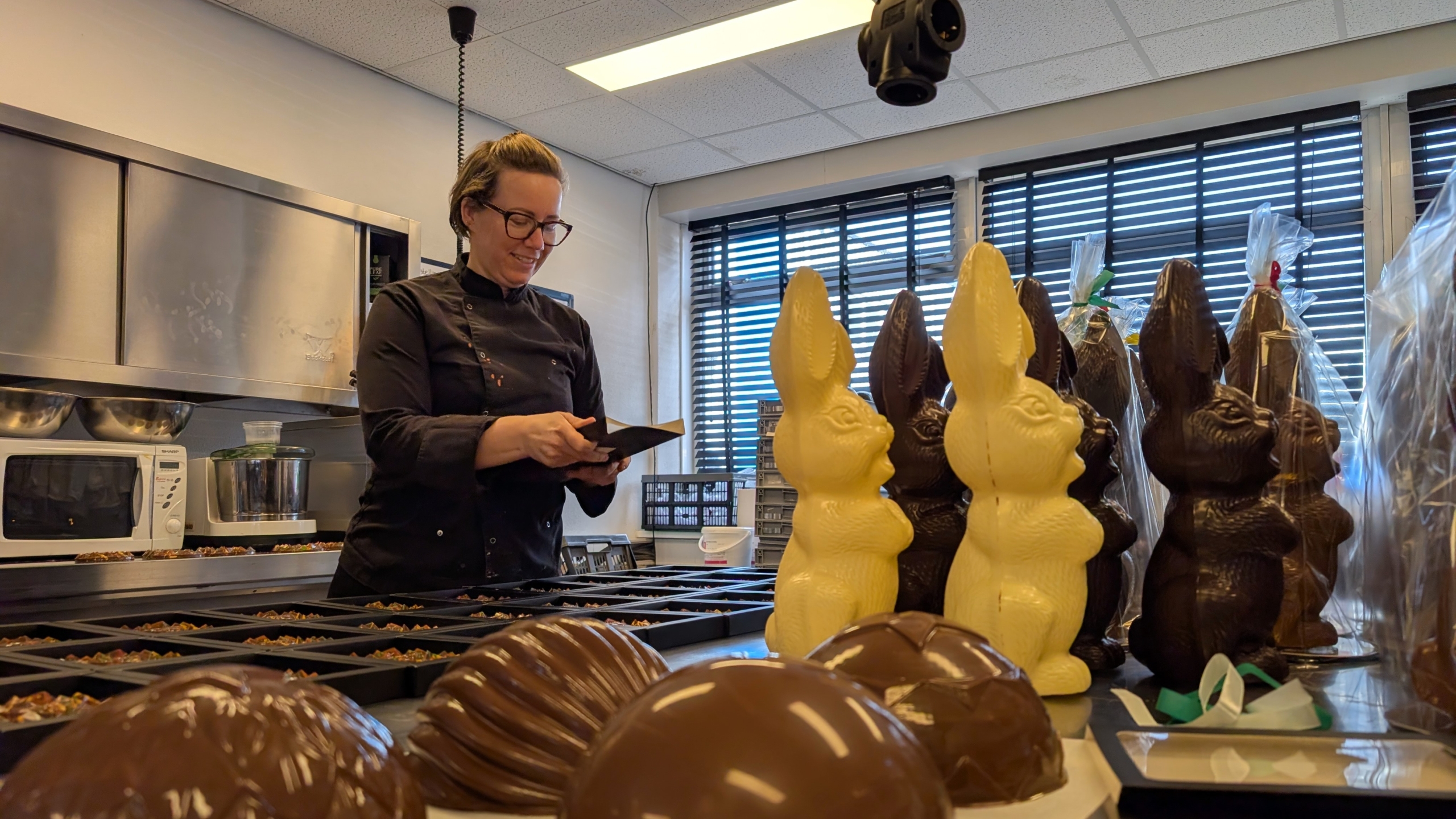 Een chocolademaker in een keuken werkt aan chocoladevormen naast grote chocoladen paashazen.