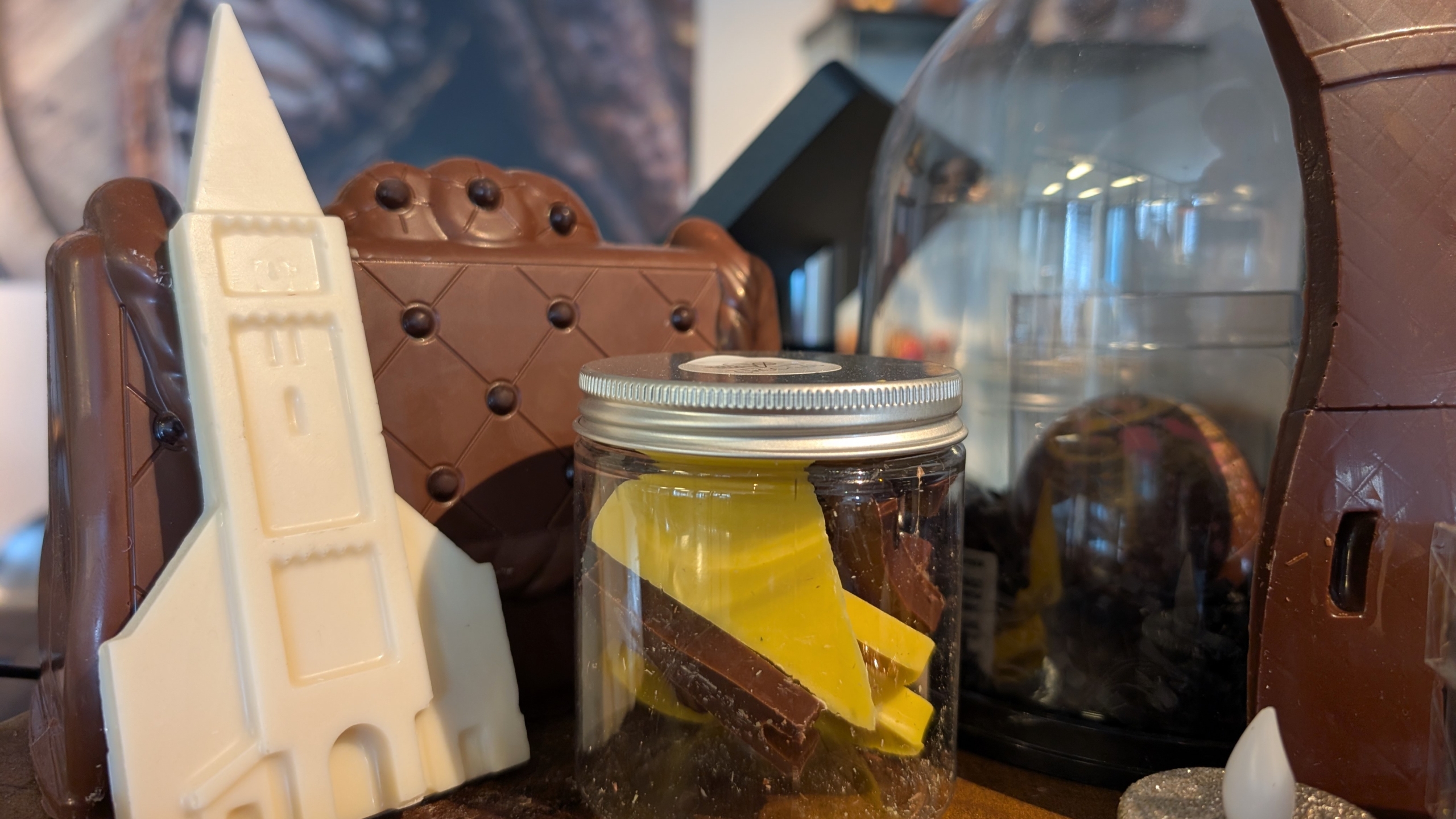 Een pot met bruine en gele chocoladestukjes, naast een witte en een bruine chocoladevorm van een gebouw.