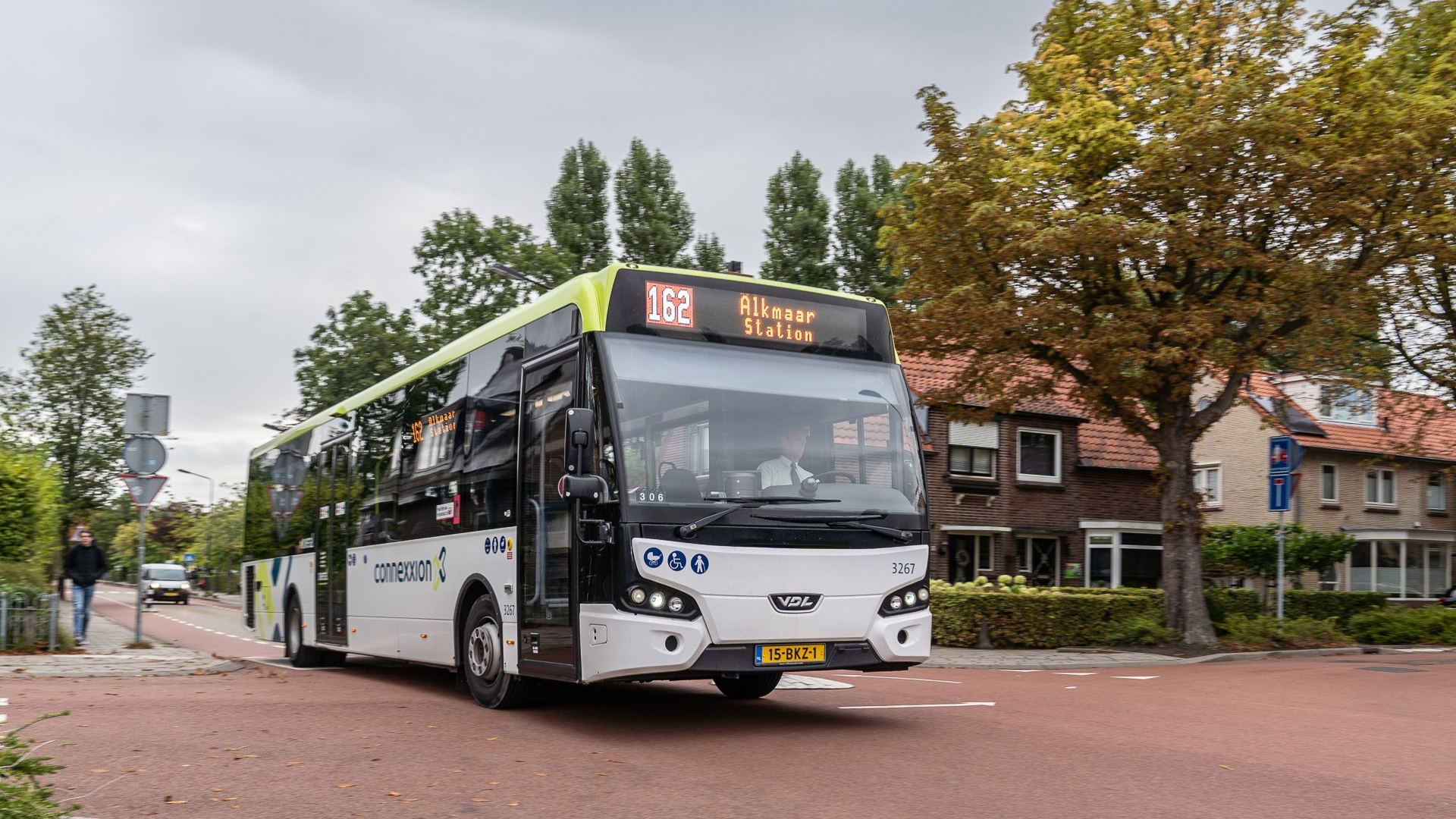 Bus 162 naar Alkmaar Station rijdt door een rustige, met bomen omzoomde straat met huizen op de achtergrond.