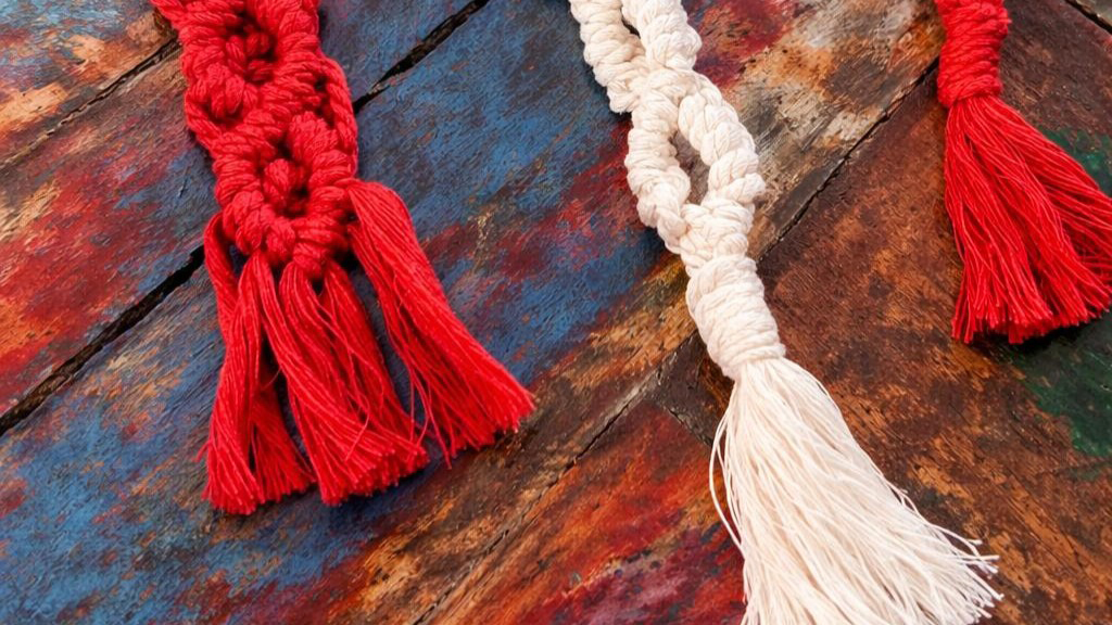 Rode en beige macramé sleutelhangers met franjes liggen op een kleurrijke houten achtergrond.