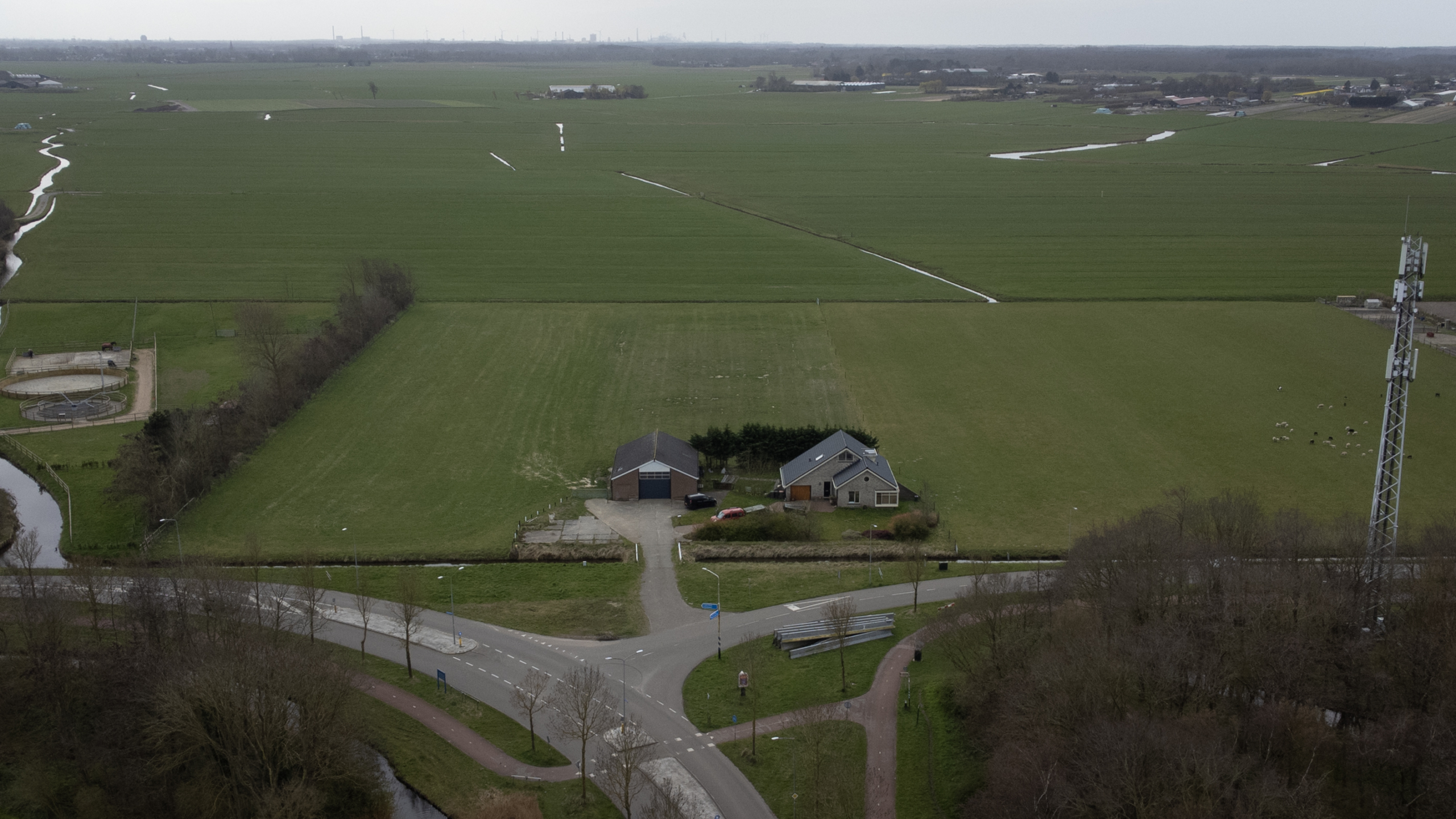 Boerderij en schuur op een groot groen veld met daarnaast een zendmast, omringd door landelijke wegen en velden.