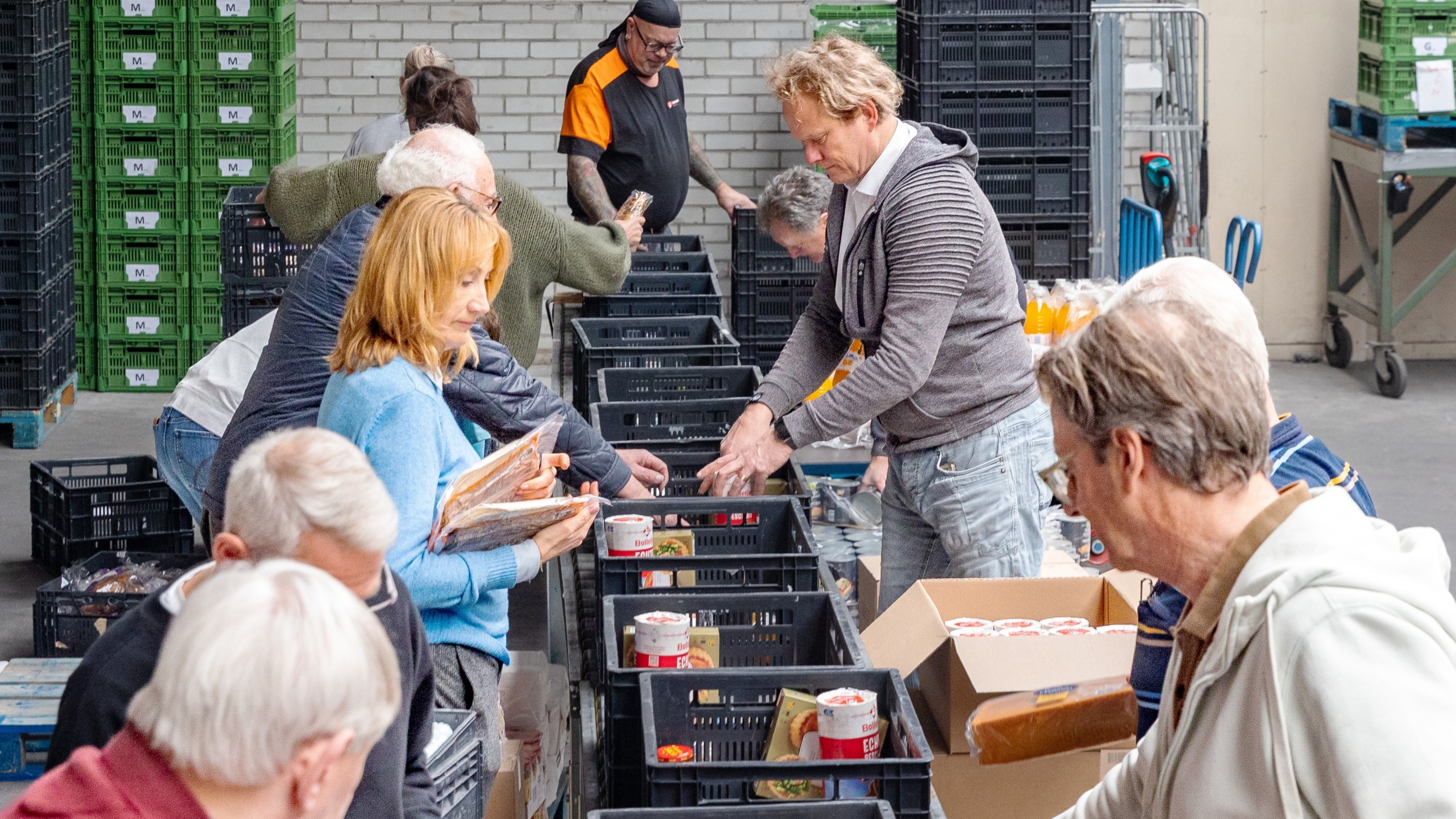 Vrijwilligers sorteren voedsel en goederen in zwarte kratten in een magazijn.