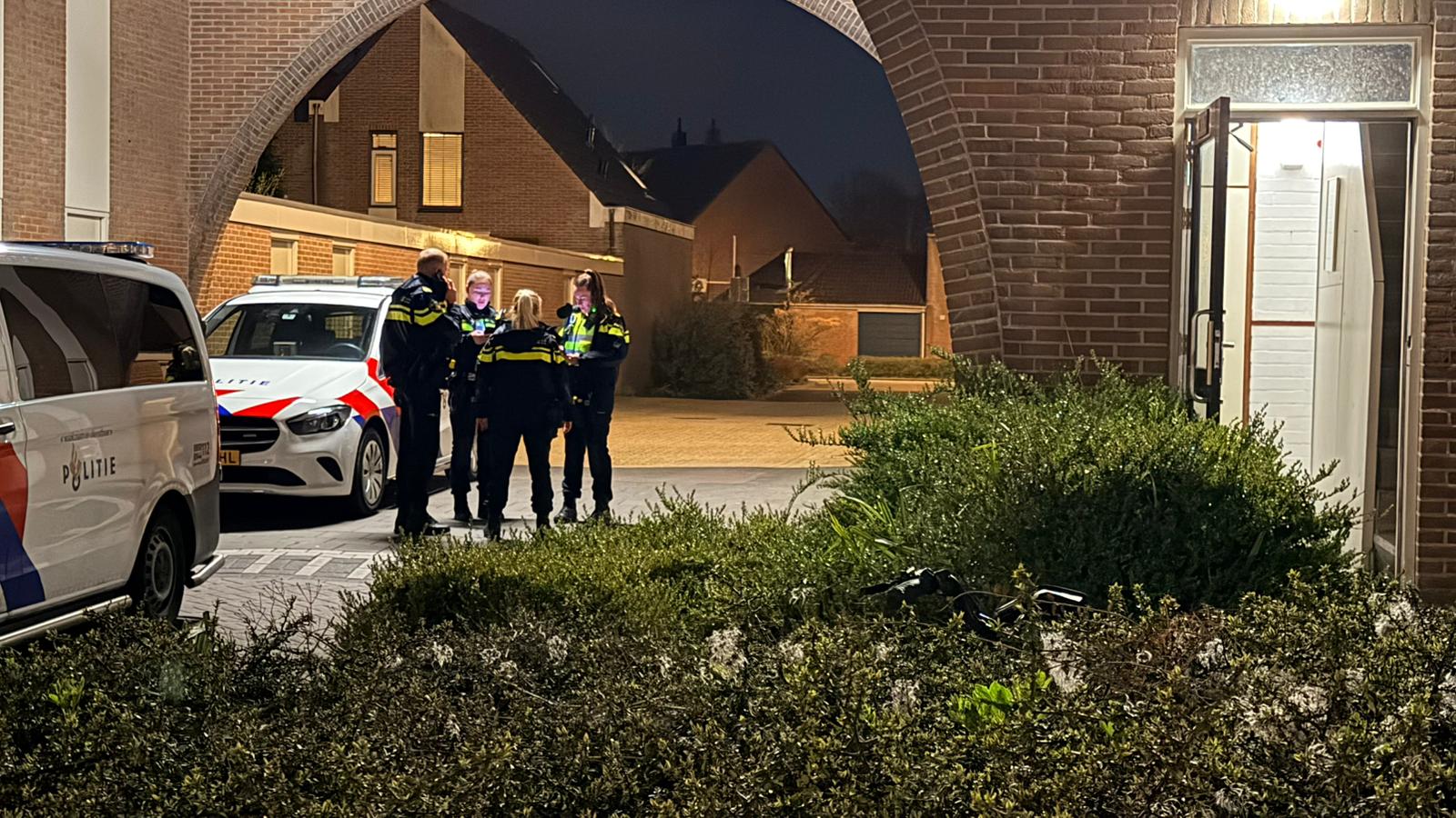 Politieagenten staan 's nachts bij politieauto's voor een gebouw met een open deur.