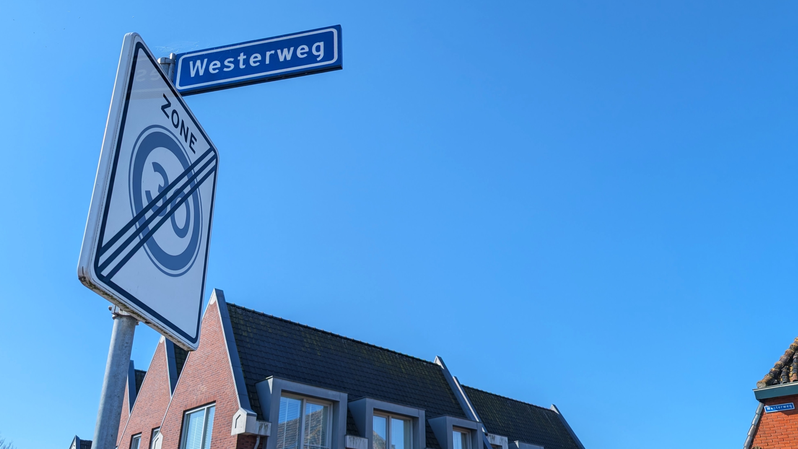 Verkeersbord met tekst "zone 30" doorgestreept en straatnaambordje "Westerweg" tegen een blauwe lucht.