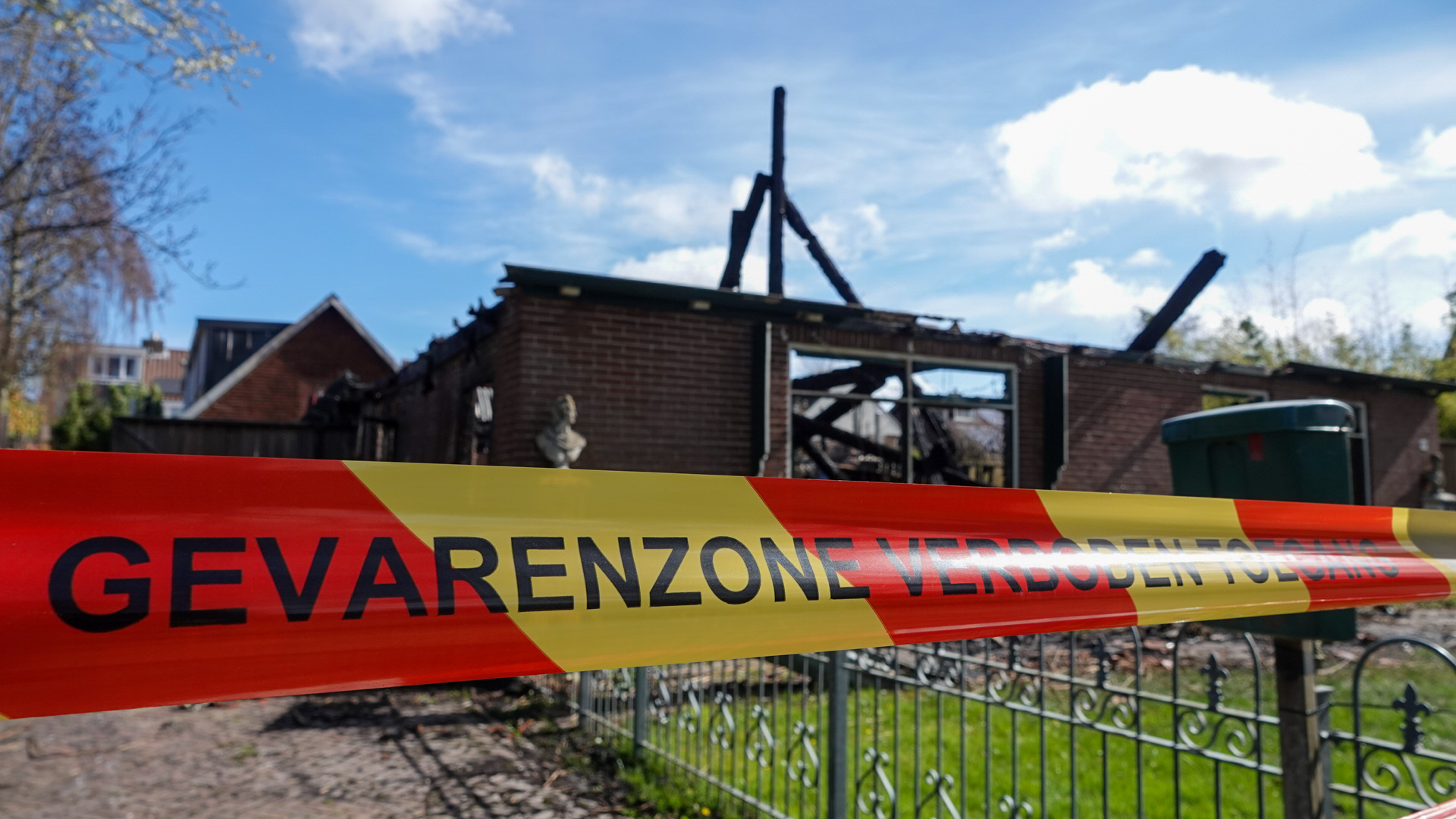 Een afgebrand gebouw omgeven door een rood-geel lint met de tekst "GEVARENZONE VERBODEN TOEGANG".