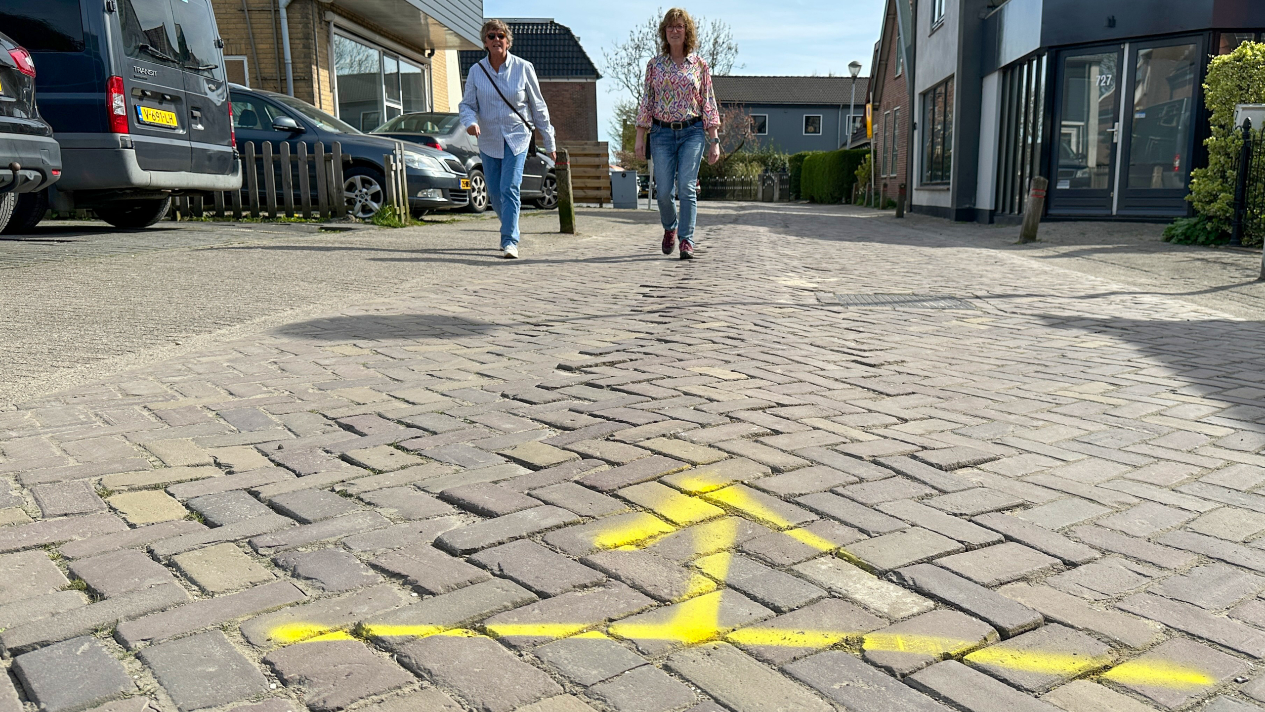 Twee mensen wandelen op een met stenen geplaveide straat met een gele pijl op de grond.