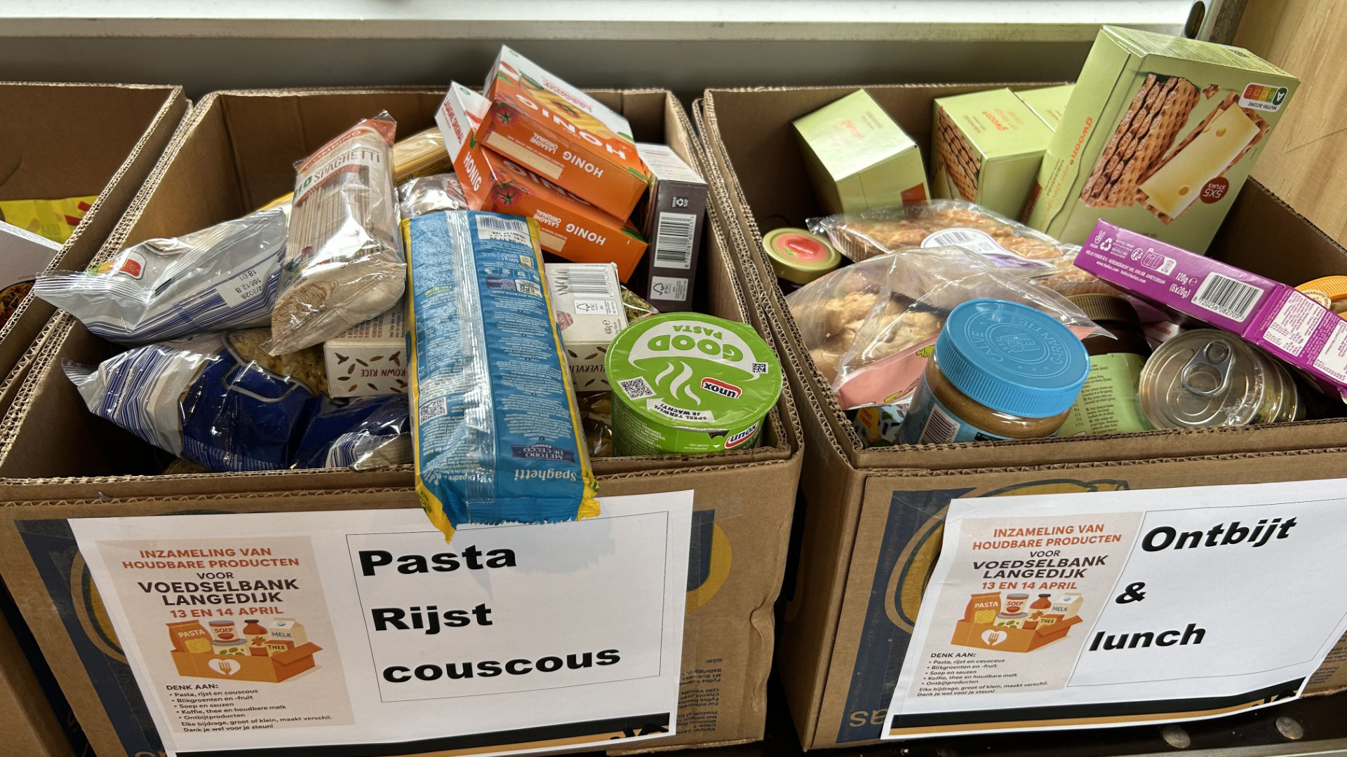 Dozen gevuld met houdbare etenswaren zoals pasta, rijst en ontbijtproducten, bestemd voor een voedselbankinzameling.