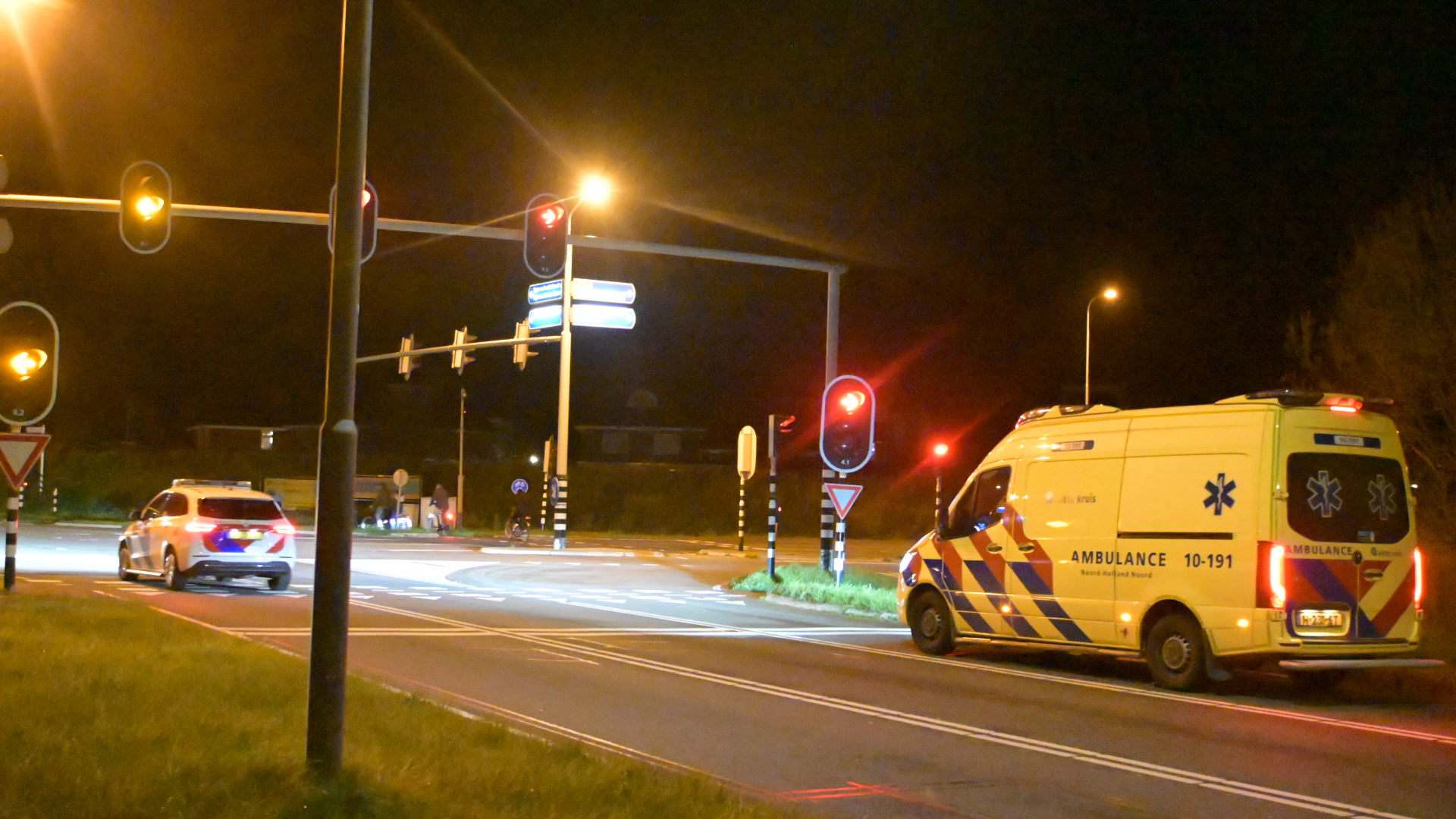 Een ambulance en een politiewagen bij een kruispunt met verkeerslichten 's nachts.