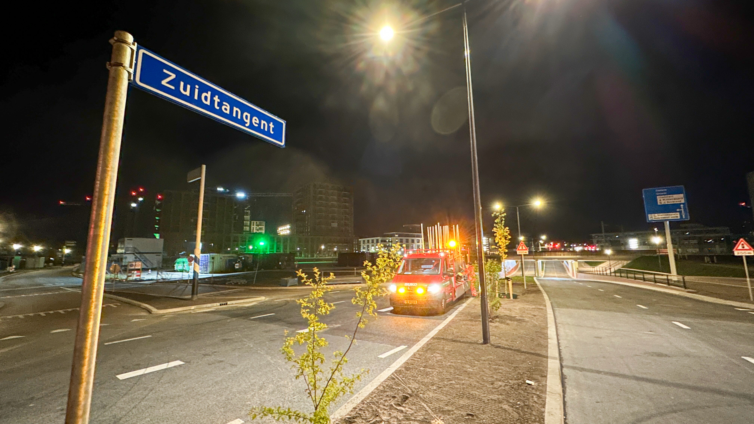 Nachtelijke straat met een verlichte lantaarnpaal, een wegwijzer "Zuidtangent," en een geparkeerde rode bedrijfswagen.