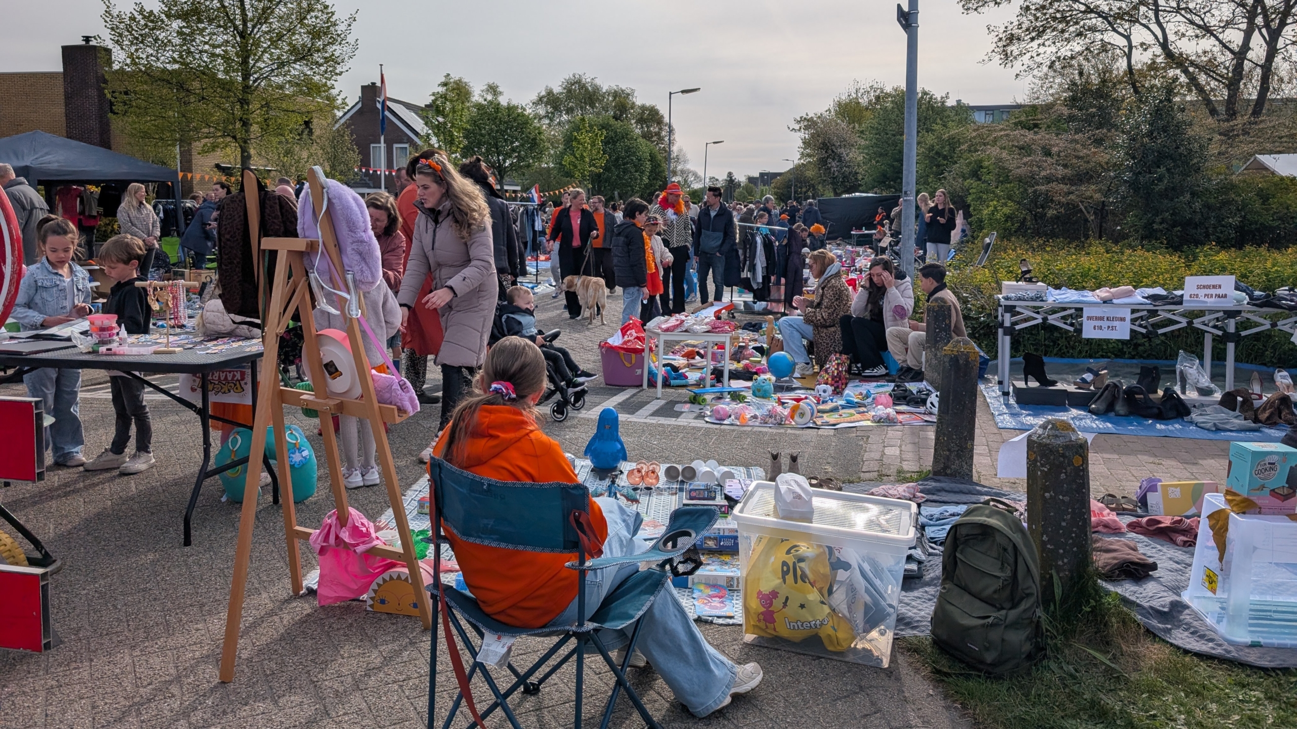 Mensen kopen en verkopen tweedehands goederen op een rommelmarkt, met tafels vol spullen en bezoekers die rondkijken.