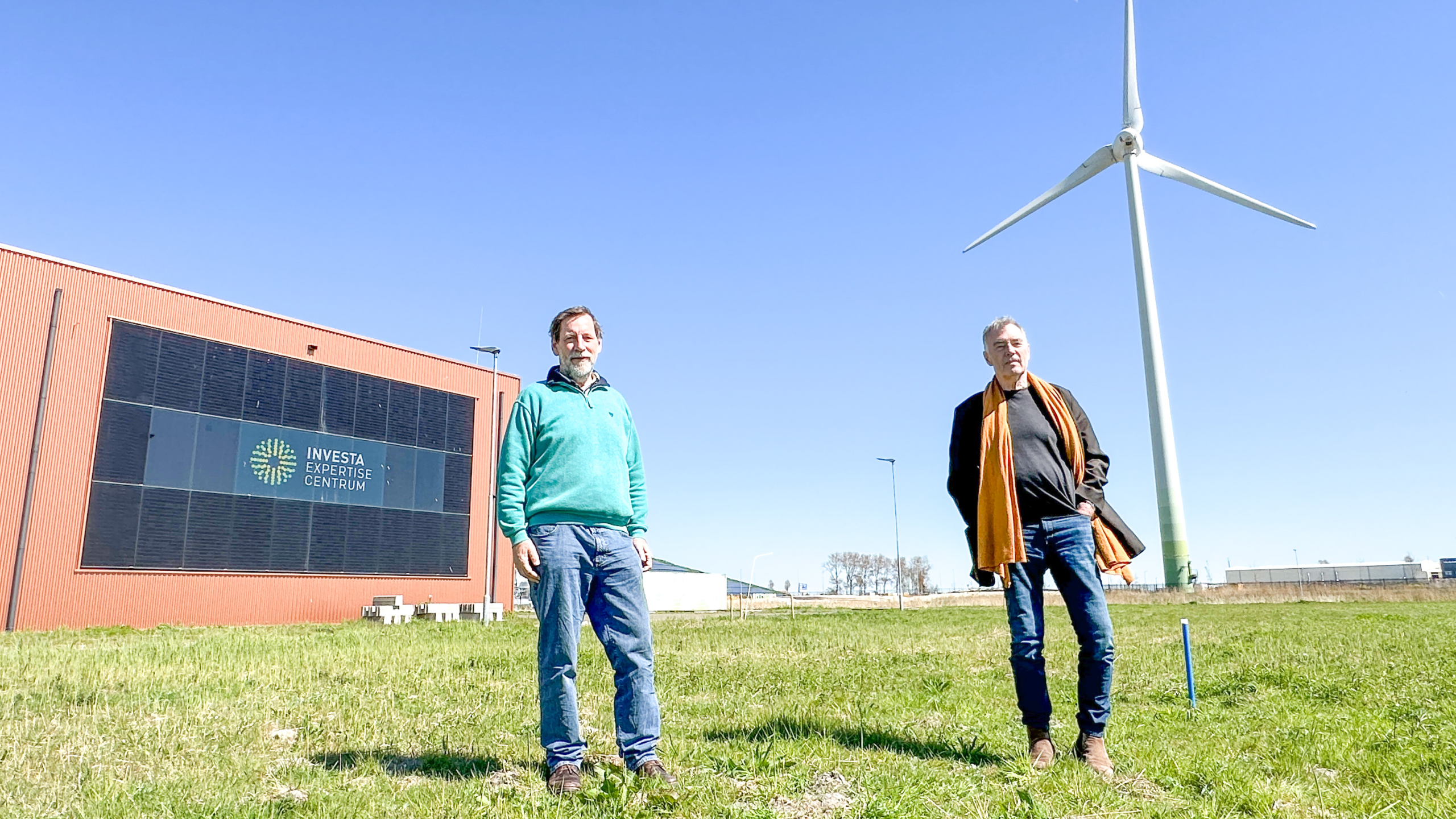 Twee mannen staan buiten bij een windturbine en het Investa Expertise Centrum op een zonnige dag.