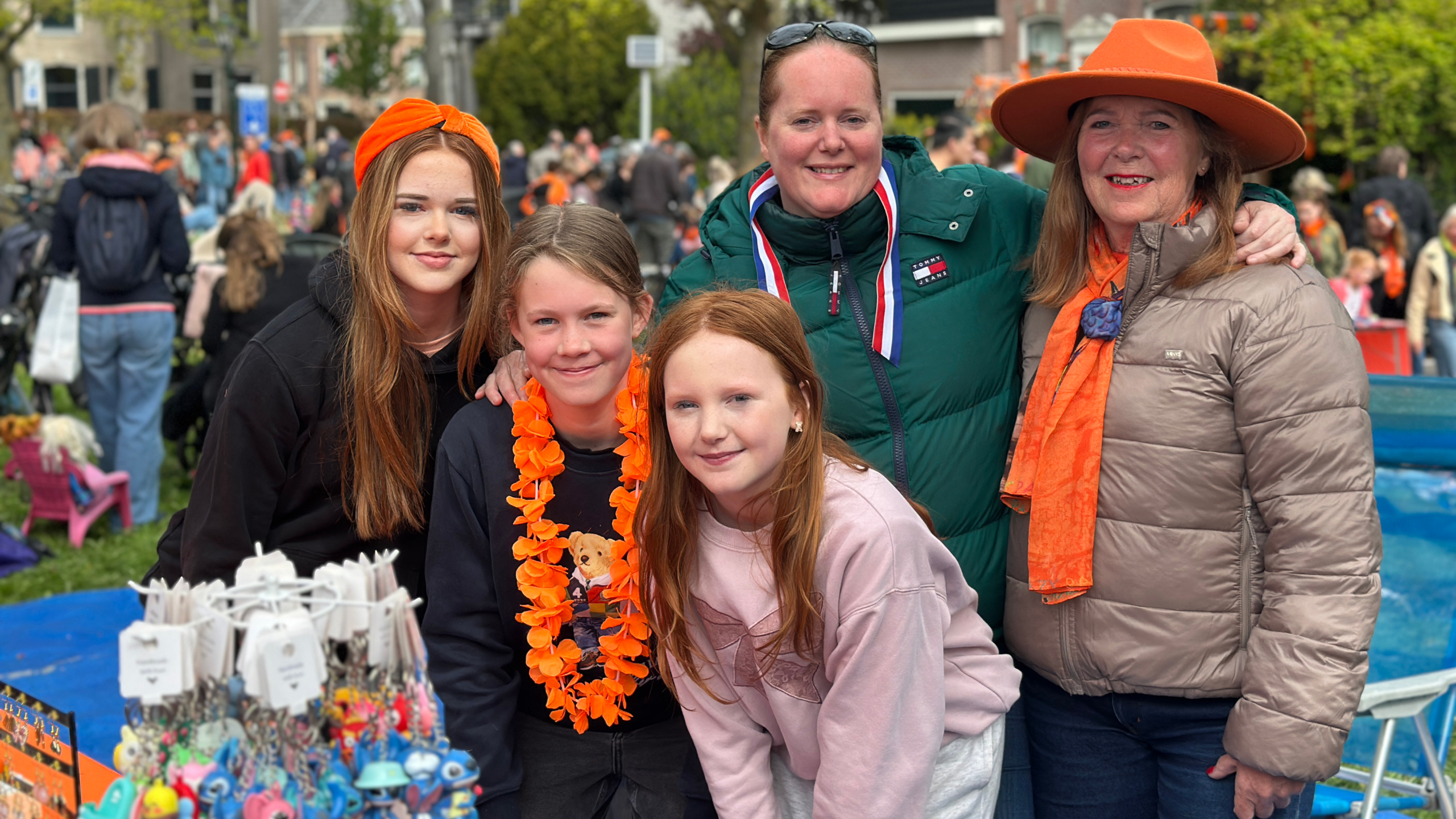 Groep mensen in oranje kleding bij een feestelijke markt, met op de voorgrond verschillende kleurrijke souvenirs.