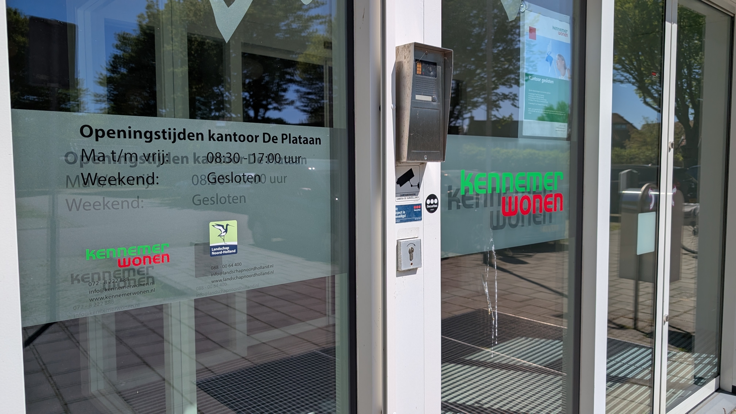 De ingang van het kantoor van Kennemer Wonen met openingstijden vermeld op de deur: maandag t/m vrijdag 08:30-17:00, weekend gesloten.