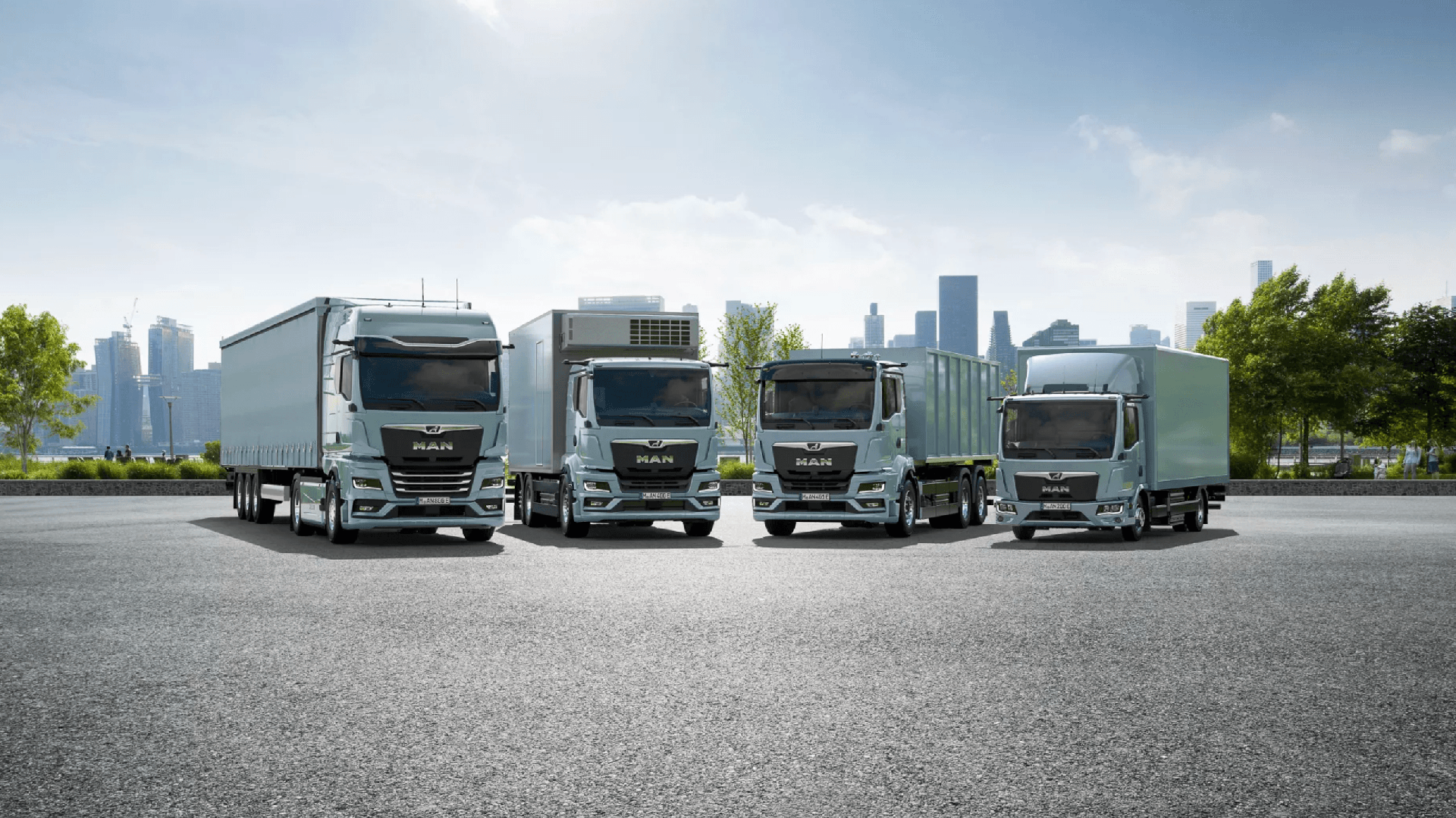 Vier vrachtwagens van het merk MAN staan geparkeerd op een open plek met een stedelijke skyline op de achtergrond.