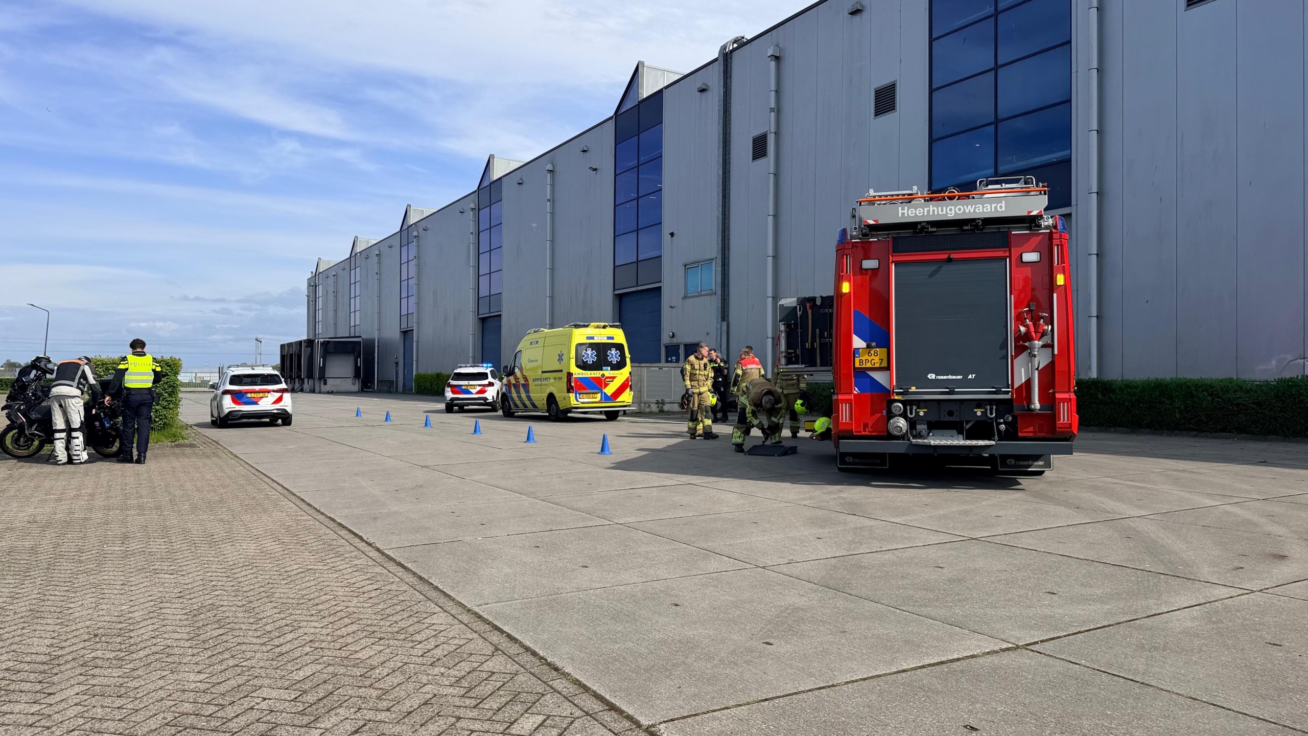 Politie, brandweer en ambulance staan buiten een groot gebouw geparkeerd; agenten en brandweerlieden zijn actief.